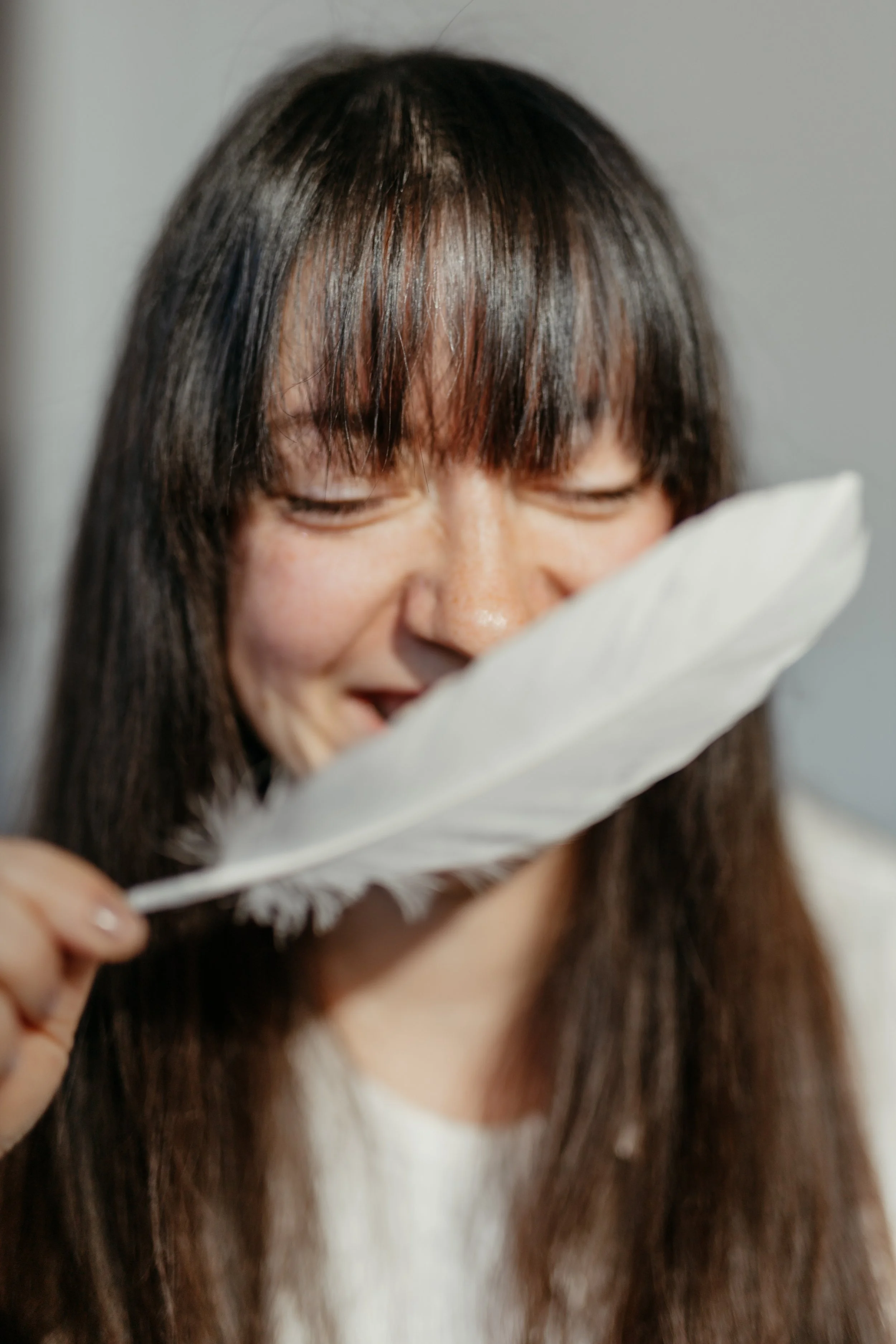 Eine lachende Person mit dunklen Haaren, die eine weiße Feder hält.