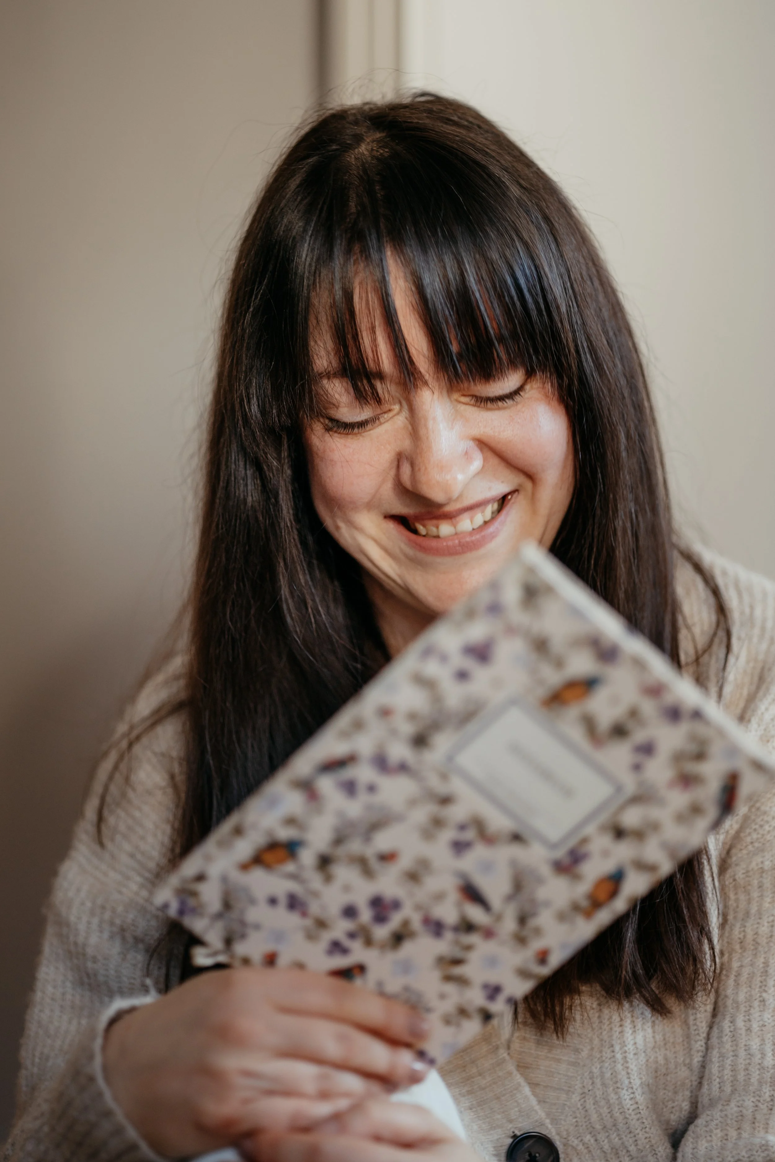 Eine lachende Frau mit dunklem Haar, die ein Geschenkpapier mit Blumenmuster hält.