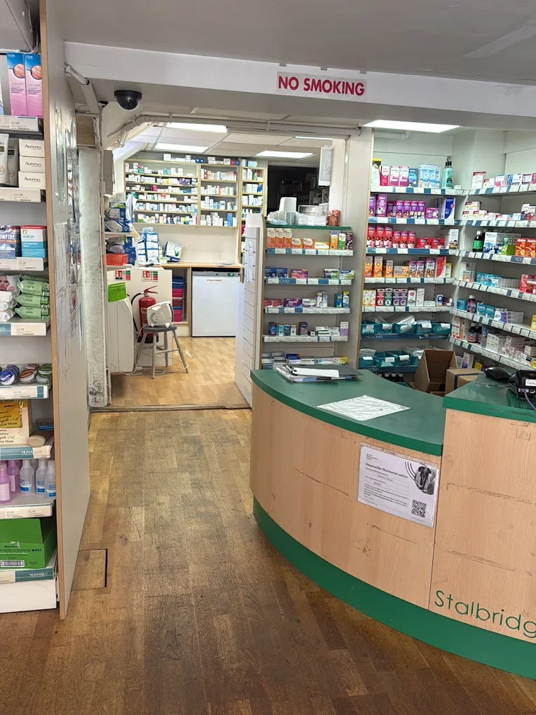 Interior view of a pharmacy with shelves of medication, a counter with papers, and a sign that reads 'No Smoking' above the entrance to the back area.