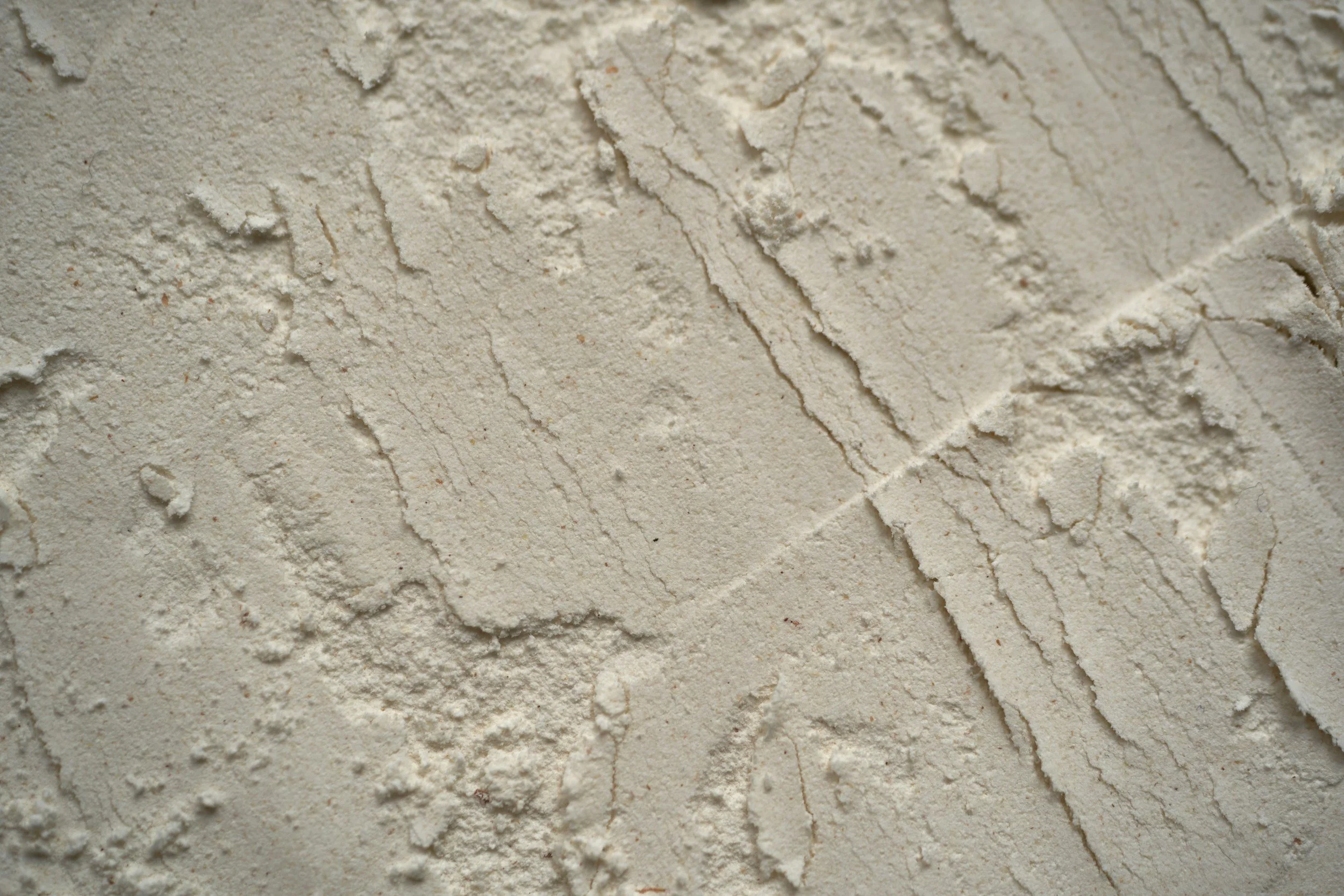 Close-up of white powdered substance with rough, uneven texture, scattered across a flat surface.