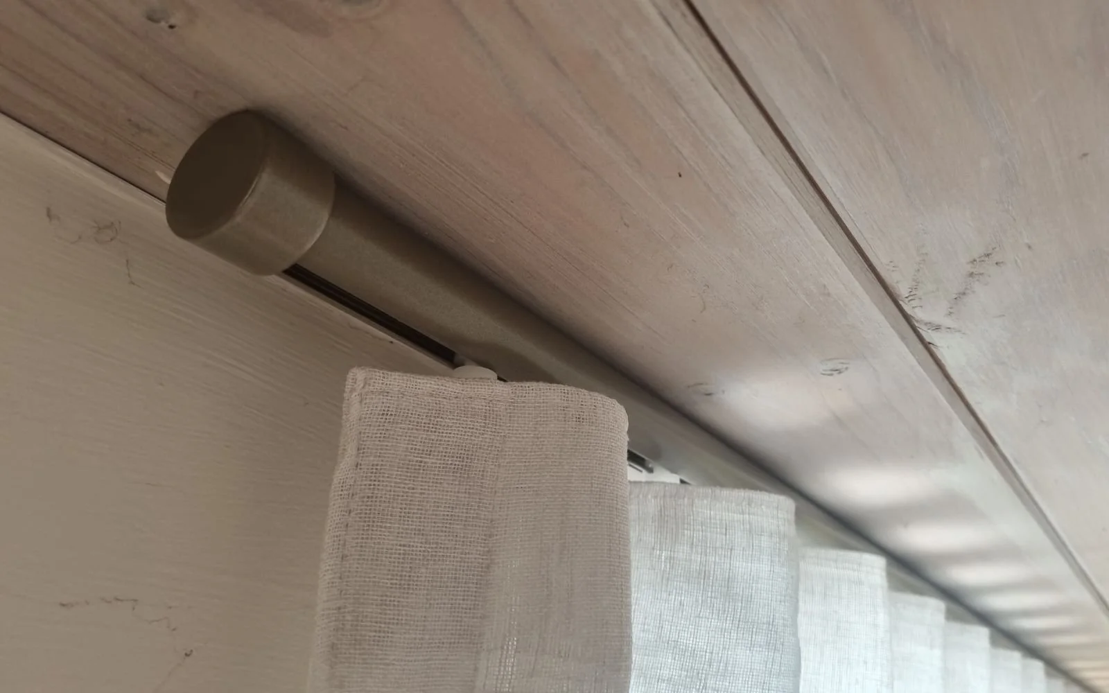 Close-up of a curtain rod mounted on a wooden ceiling, with curtains hanging down.