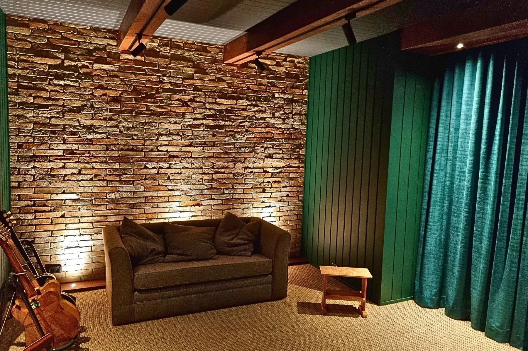 Cozy living room with exposed brick wall, green curtains, and a brown sofa with pillows, illuminated by warm lighting.