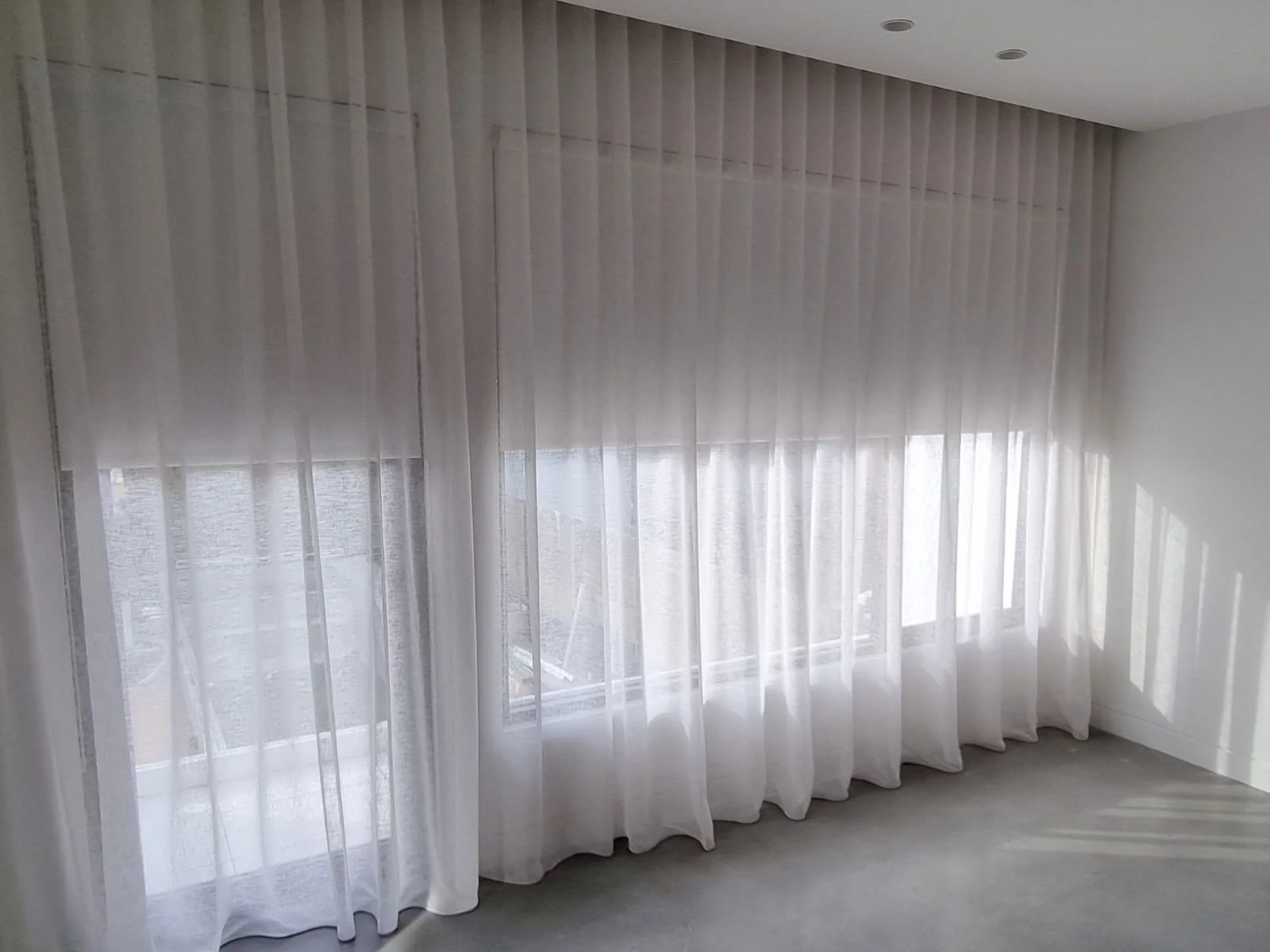 A bright room with large windows covered by sheer white curtains, sunlight streaming through.