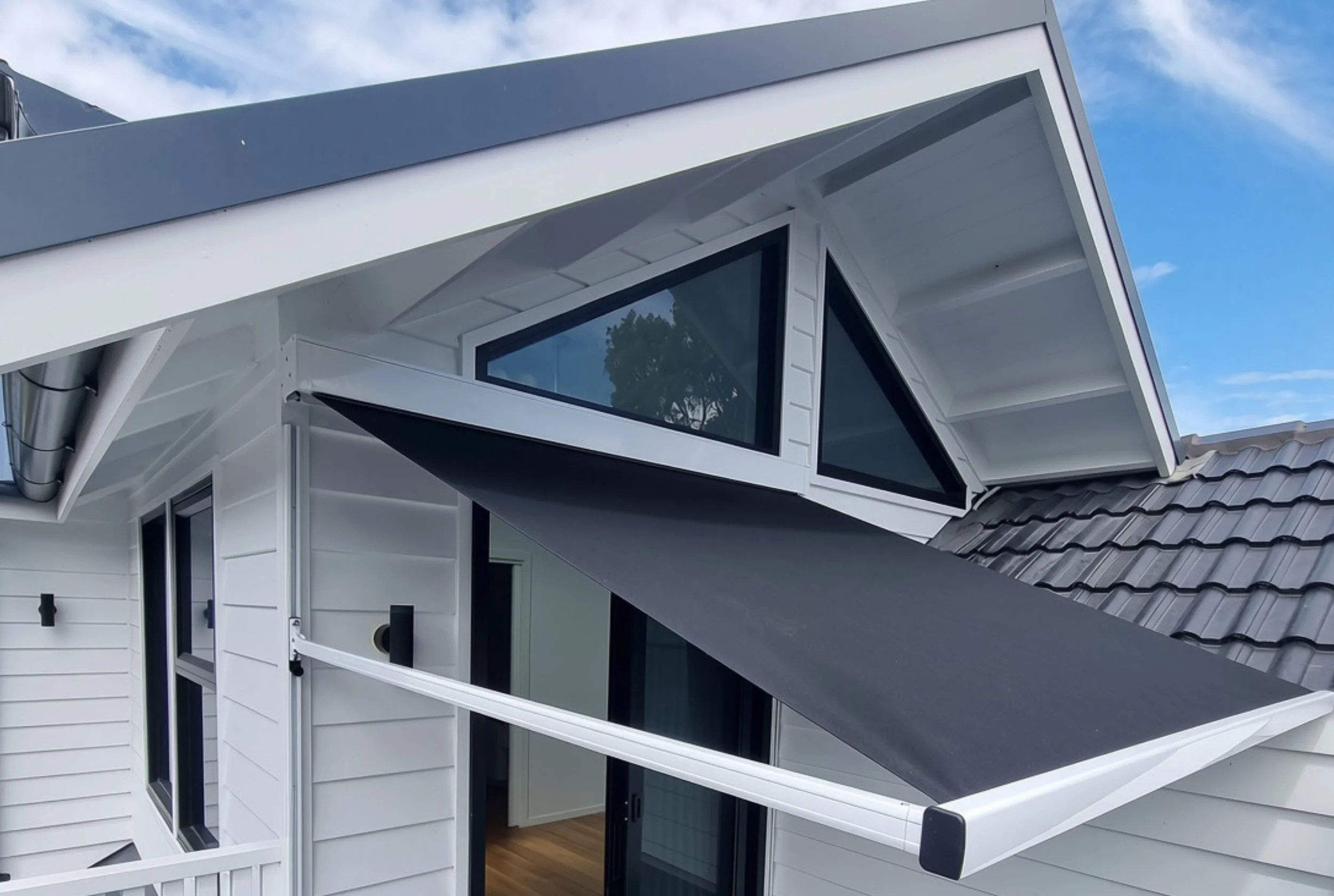 Modern house with angular design, white exterior, large windows, gray roof tiles, and a small balcony or overhang