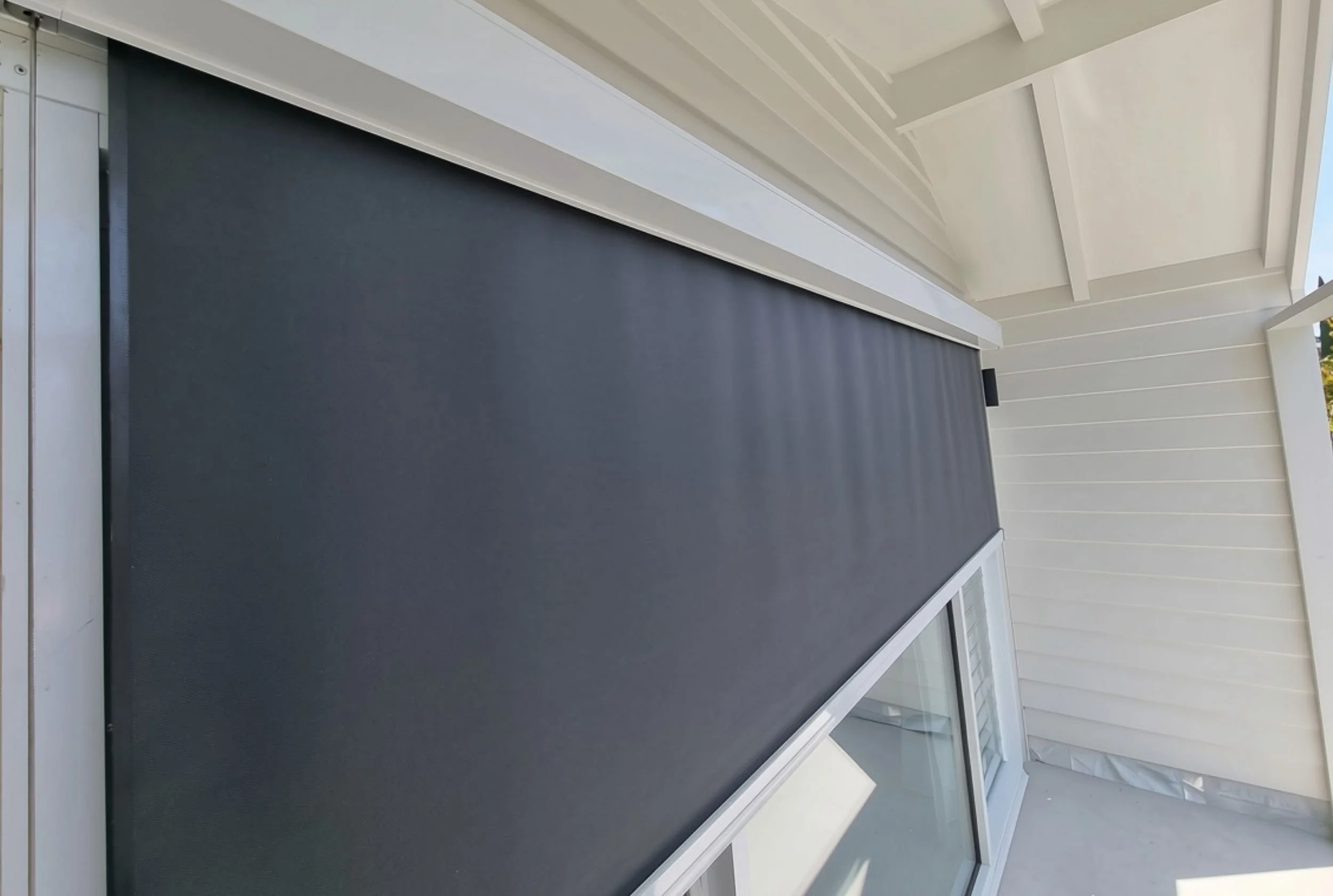 Close-up of a sliding glass door leading to a balcony with a black outdoor rug and white framing, under a white ceiling with beams.