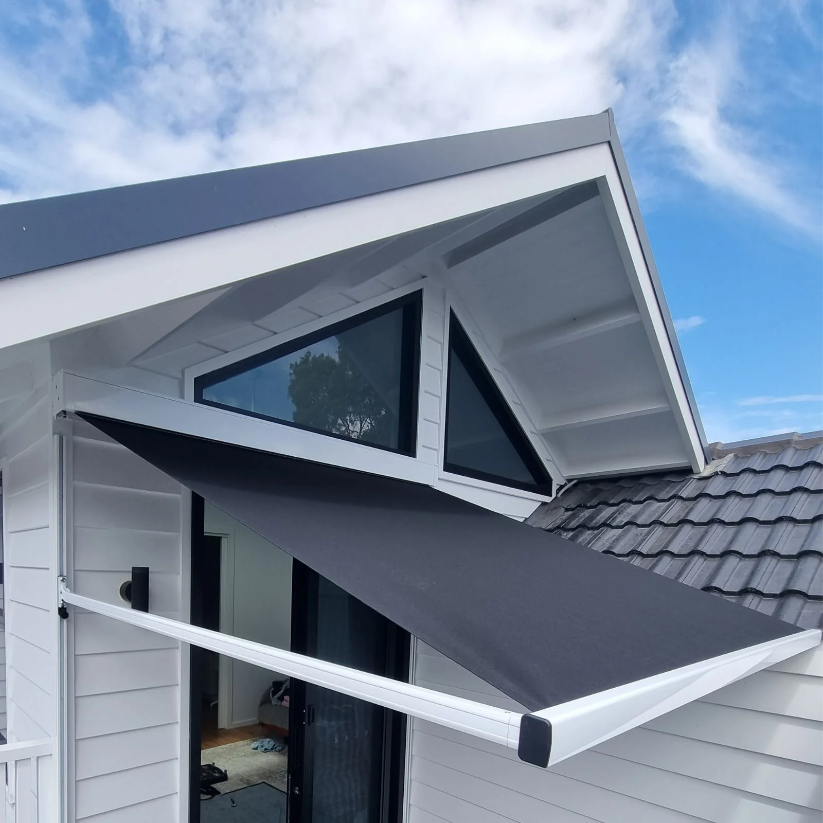 Close-up of a modern house's roof with large, angled windows and a gray roof panel, under a partly cloudy sky.