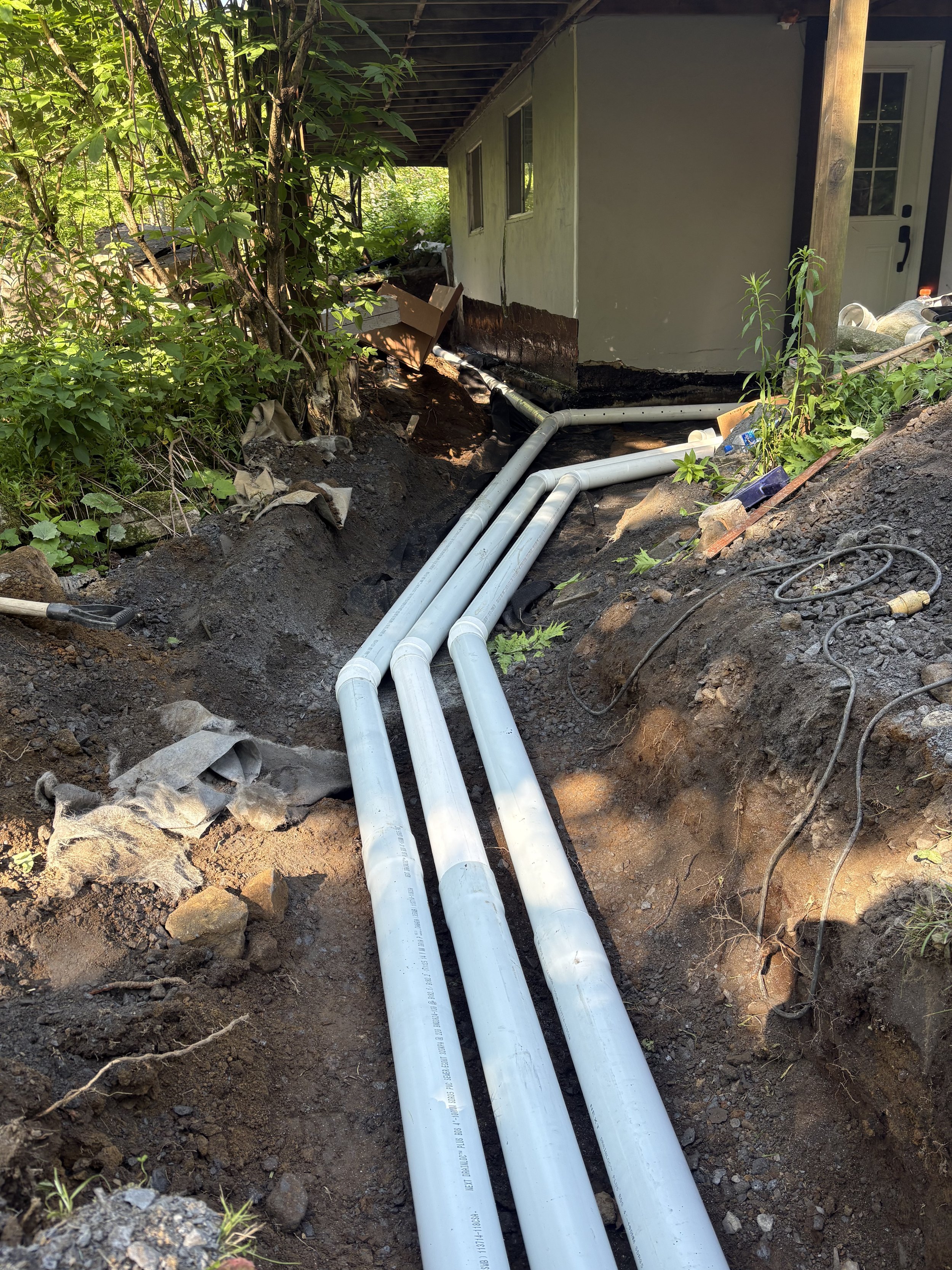 Installation de conduites d'eau en pvc souterrain devant une maison, entourée de végétation verte.
