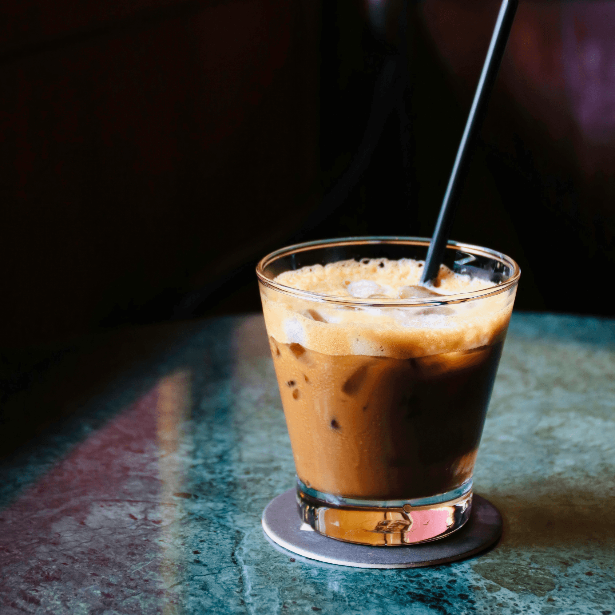 A glass of iced coffee with a straw on a textured surface.