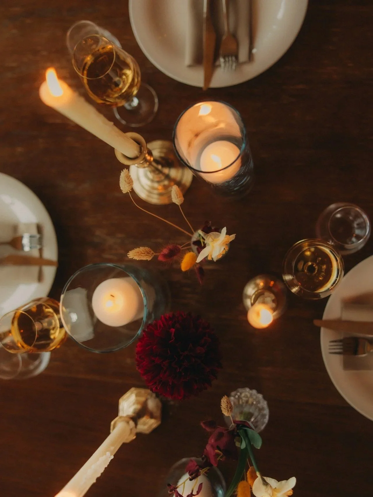 Borddekor med levende lys, vin, blomster, stearinlys, tallerkener, bestikk og glass, satt opp for en middag.
