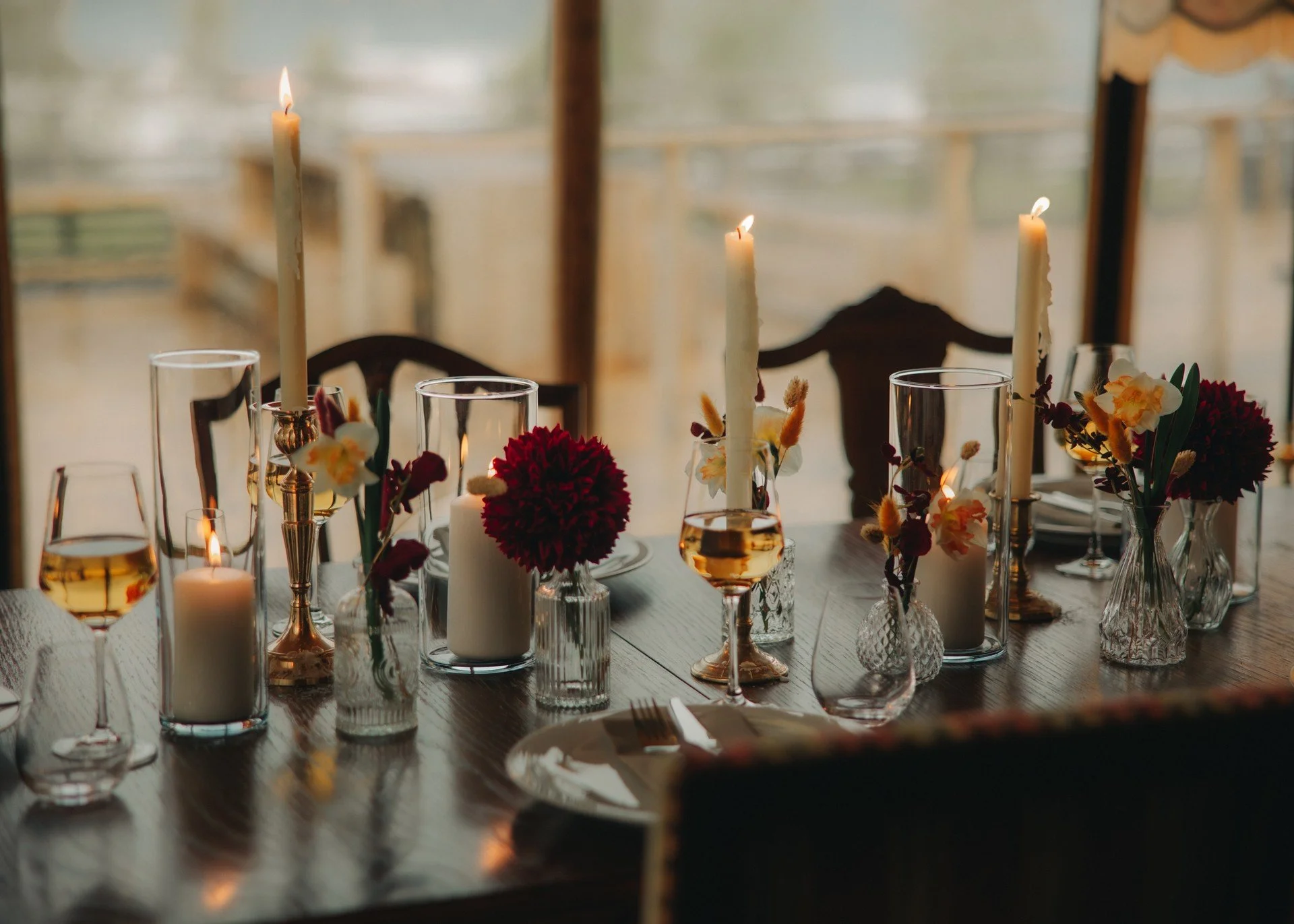 Et bord dekket med blomster, lys og glass med drikke, sannsynligvis til en formell anledning.