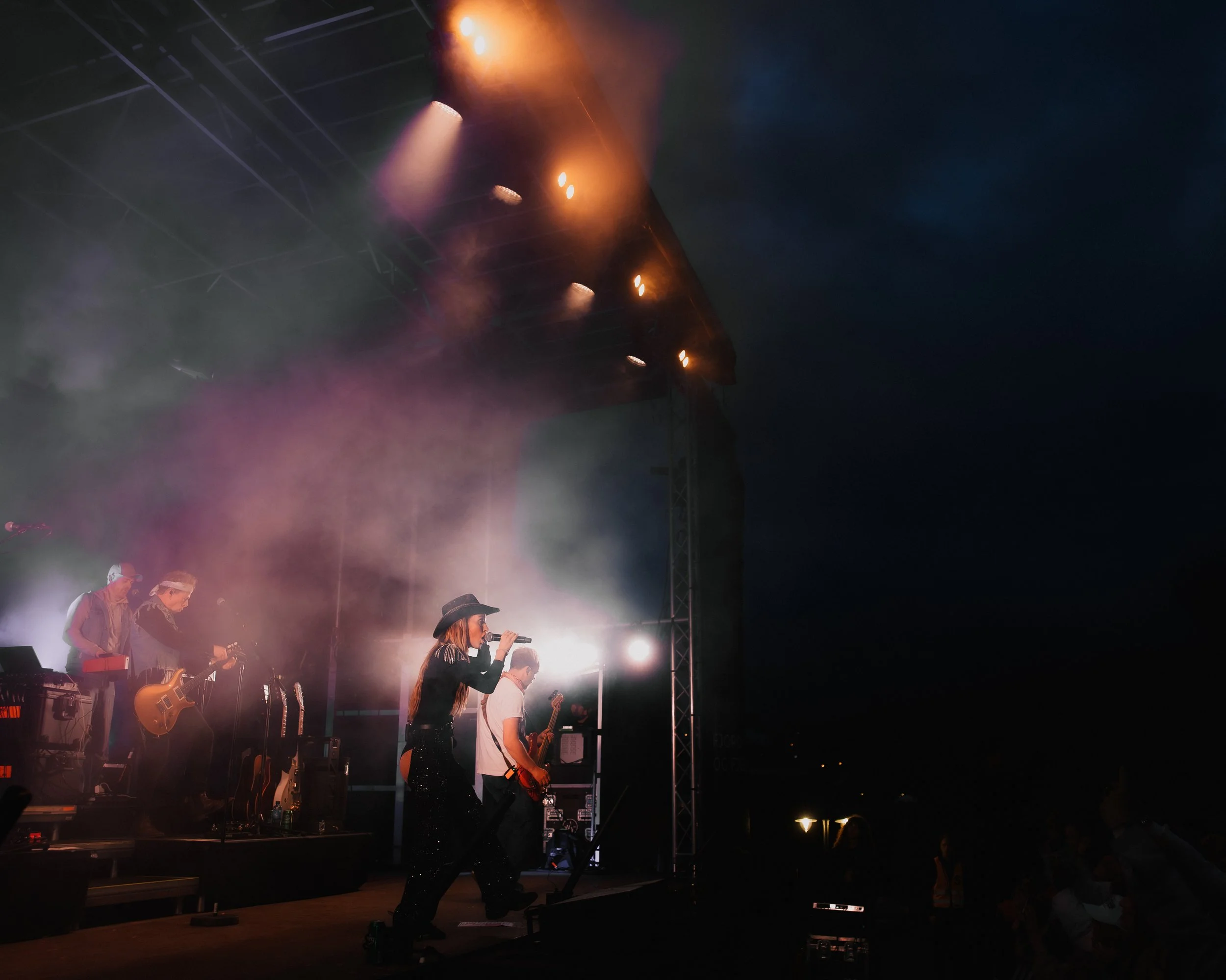 En musiker spiller gitar på en scen med flere bandmedlemmer under konserten, omgitt av scenelys og tåke.