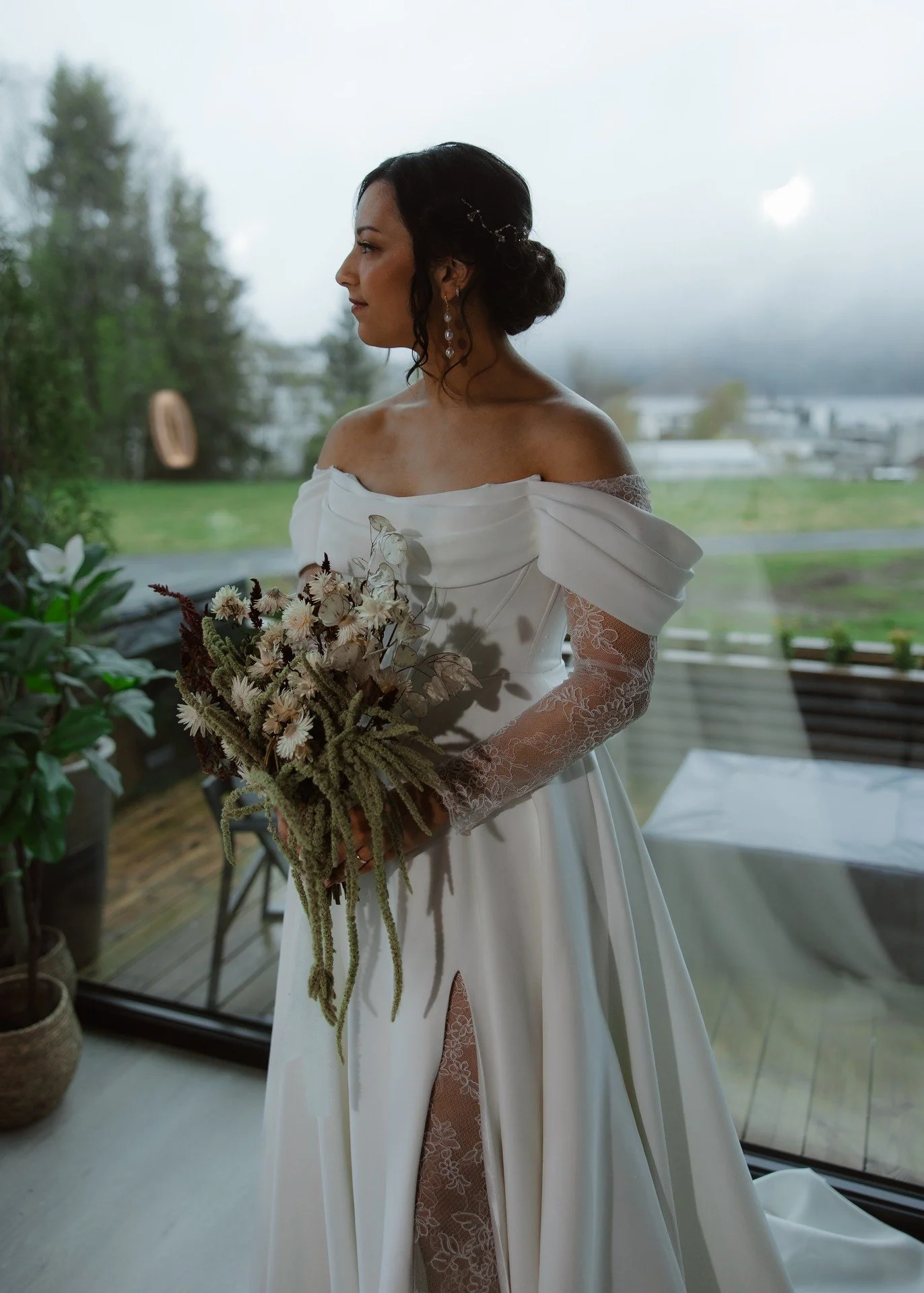 Kvinne i brudekjole som holder en blomsterbukett, sett fra siden med utsikt ut gjennom store vinduer. Merk: Alt-tekst er bare en fortolkning basert på bildet, kan ikke garantere nøyaktighet.