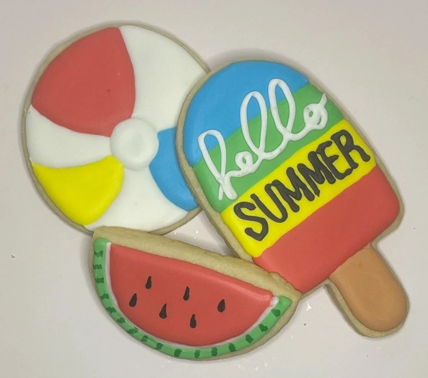 Colorful decorated sugar cookie shaped like a summer ice cream cone with a watermelon slice, beach ball, and sunscreen bottle design.