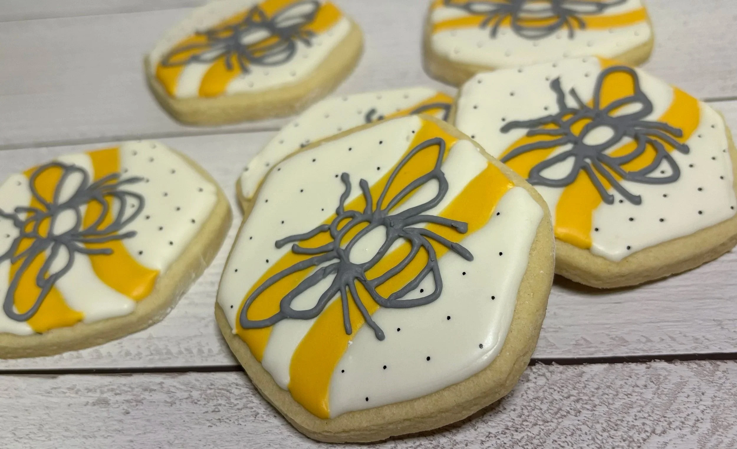 Decorated cookies with yellow, white, and gray icing, featuring a butterfly design, on a white wooden surface.