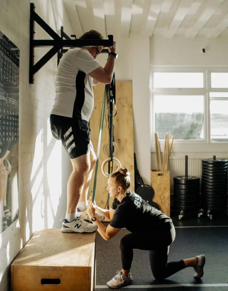 BUILT Training coach assisting a member with a banded pull-up progression