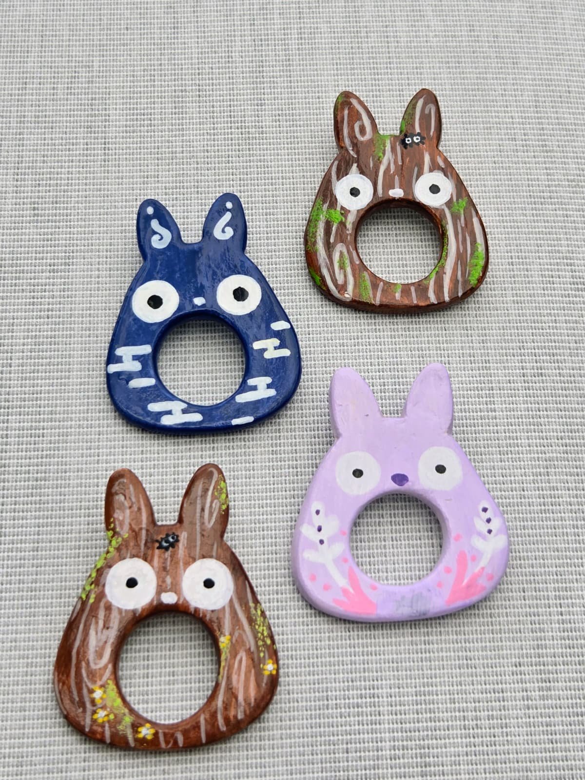 Four painted ceramic bunny-shaped pictures with open center holes, displayed on a textured beige surface. Each bunny has distinct colors and designs.