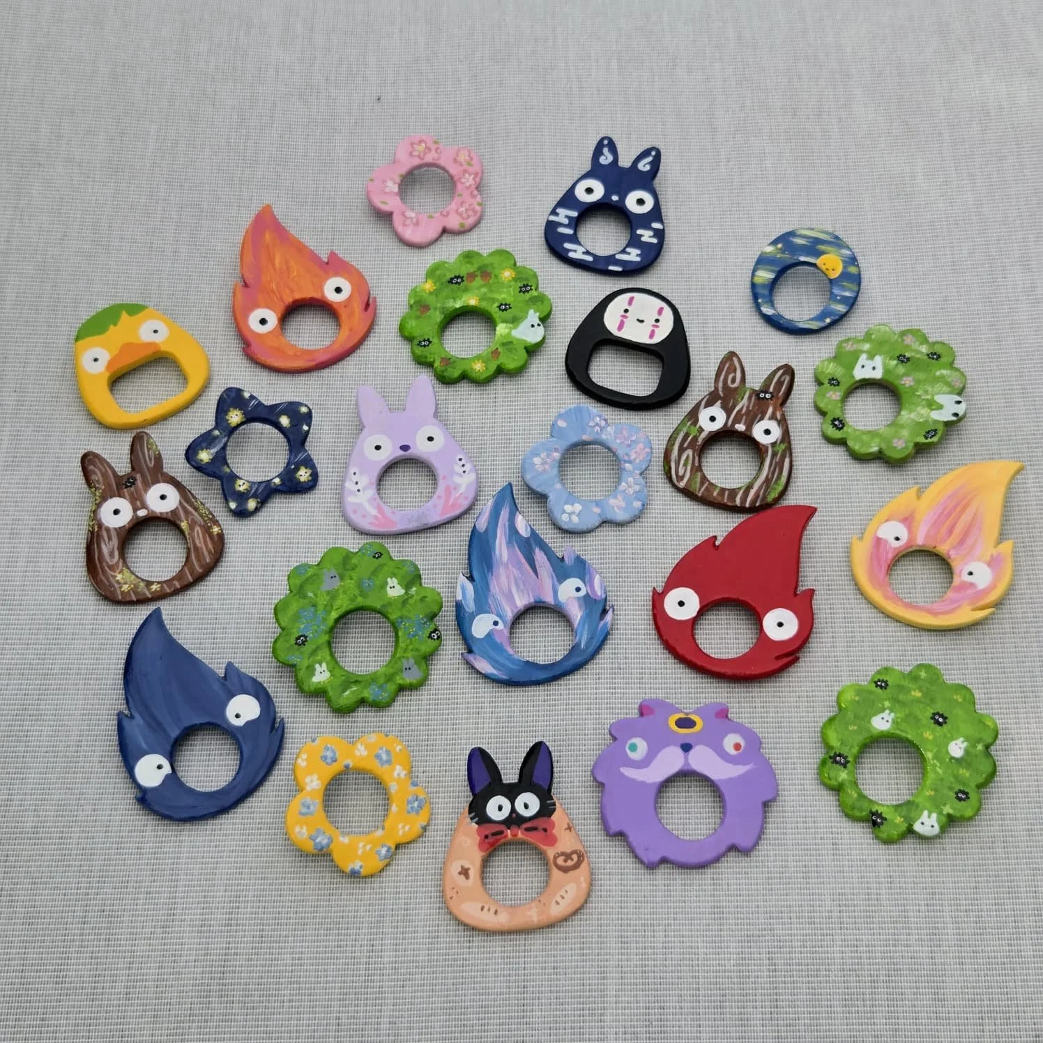 Colorful ceramic or painted rings with various creature and character designs, arranged on a light gray textured surface.