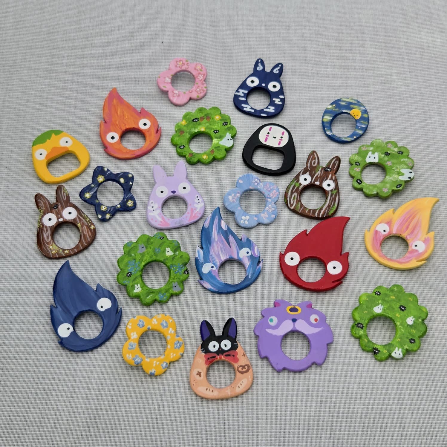 Colorful decorative ring-shaped objects with various designs, including animals and abstract patterns, arranged on a gray surface.