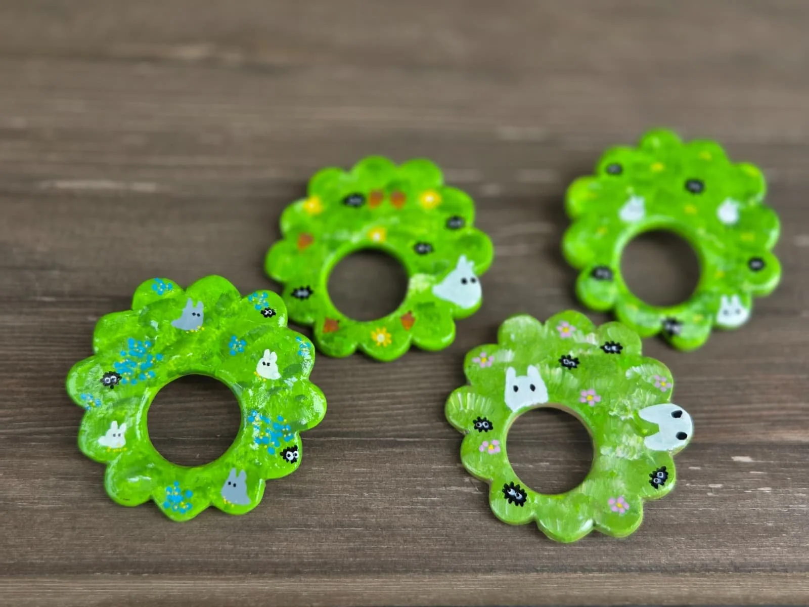 Four small, bright green, flower-shaped hair clips with cartoon bunny and floral patterns on a wooden surface.