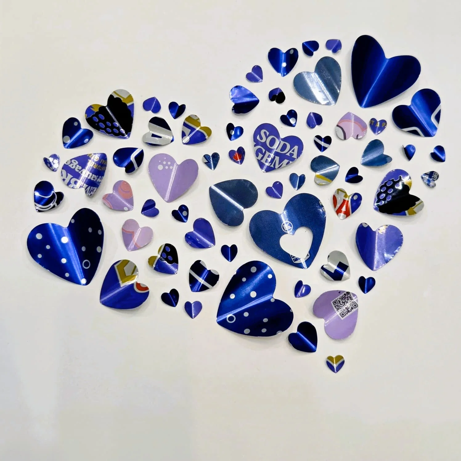 Assorted metallic and glossy paper hearts in purple, blue, silver, and pink colors scattered on a white surface.