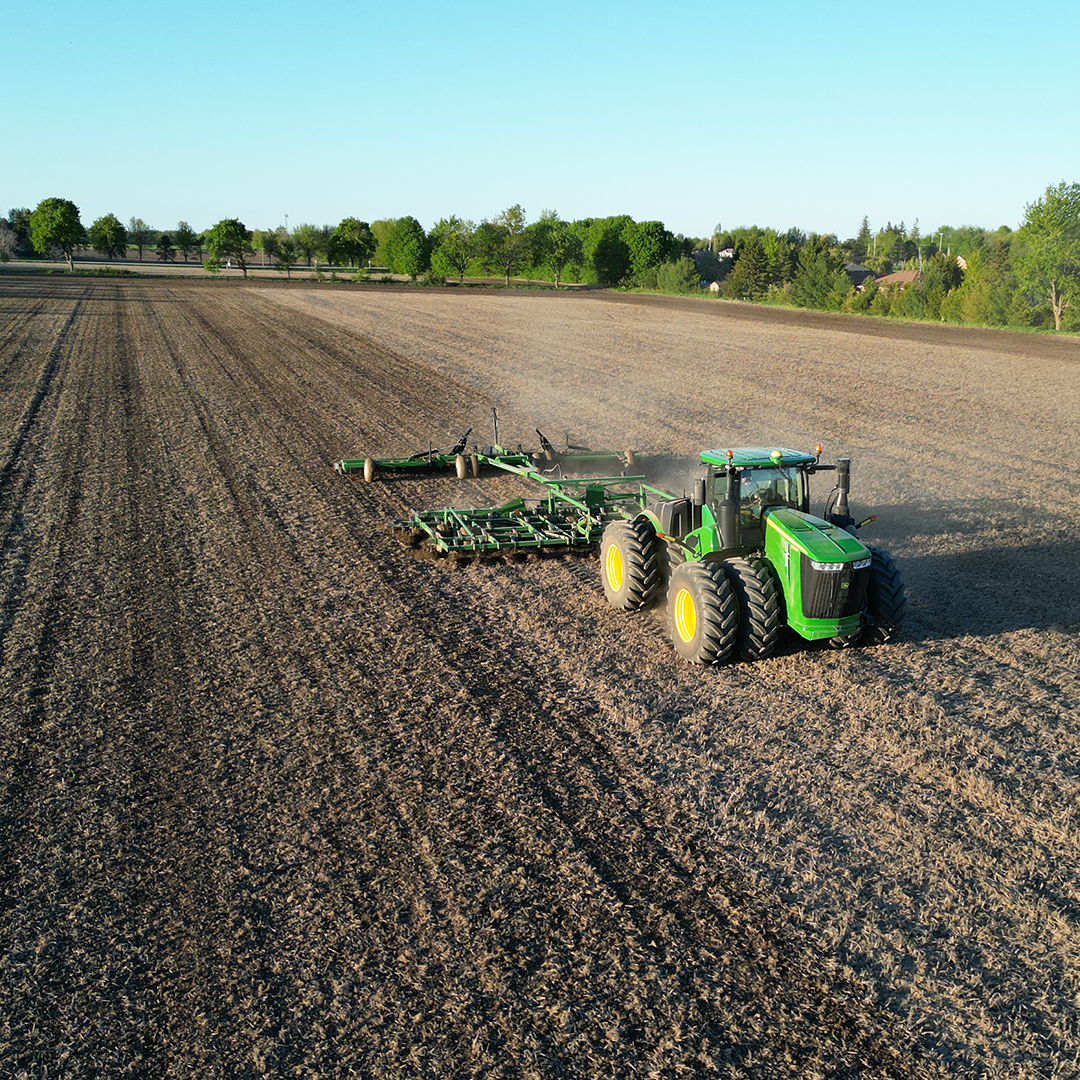 A green John Deere tractor planting on a large farmland field at sunset.