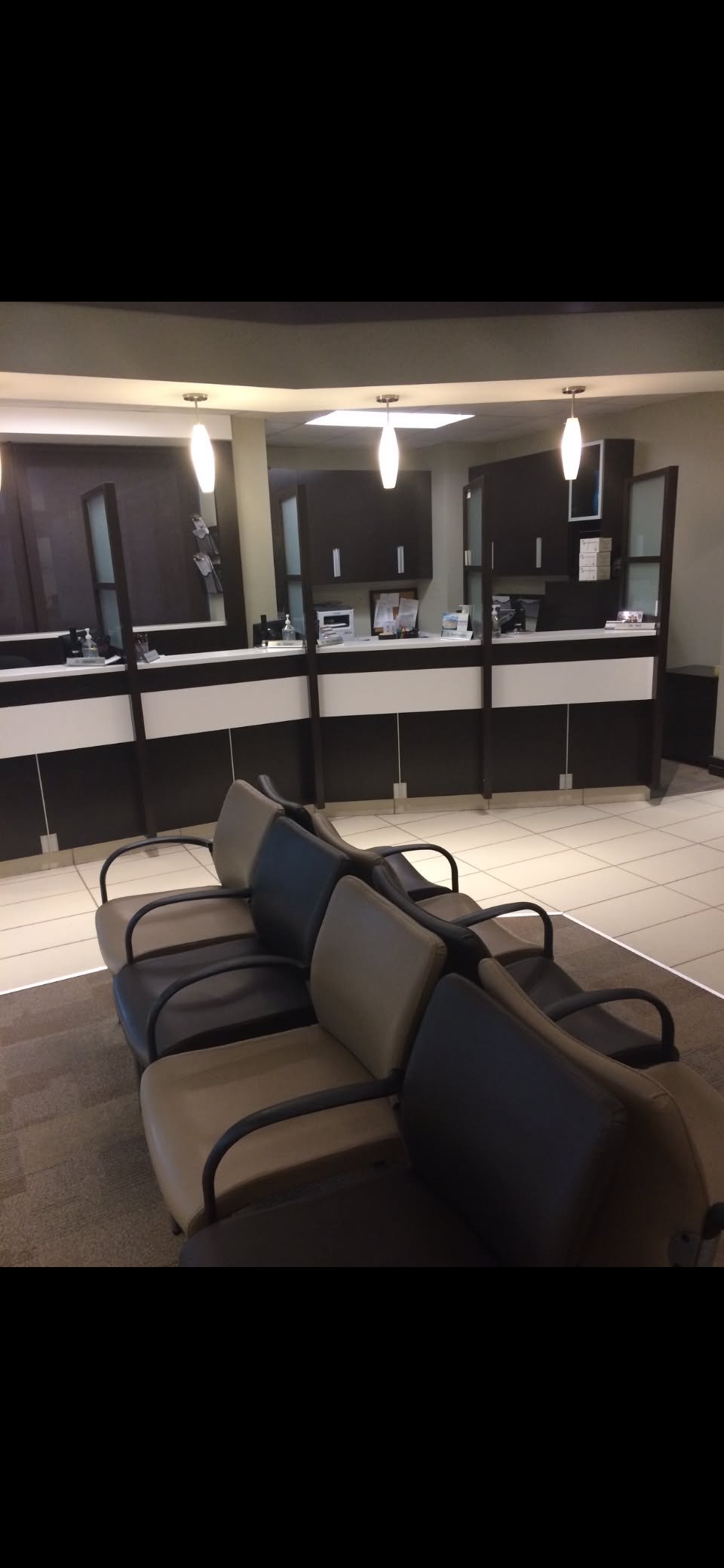 A reception area with black and white check-in counters, four chairs in the foreground, and pendant lights hanging from the ceiling.