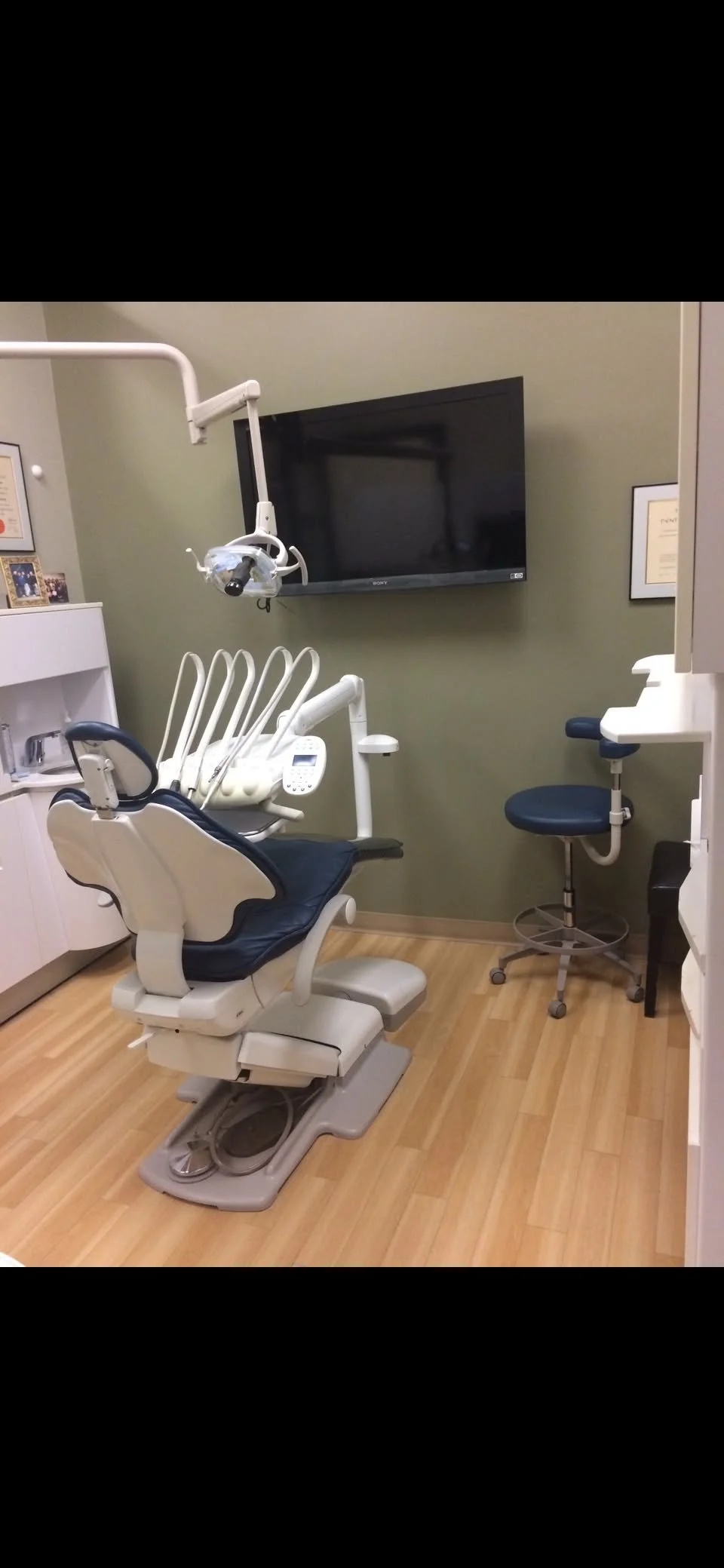 Dental office with a dental chair, overhead light, and television on the wall.