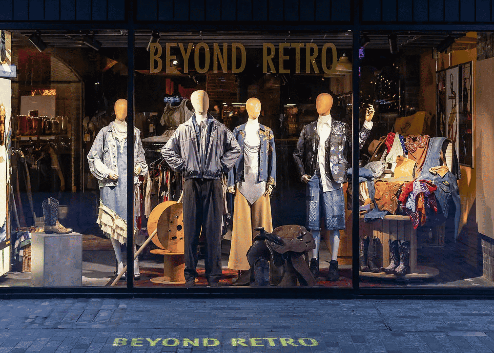 Storefront window display with mannequins dressed in vintage-style clothing, featuring jackets, skirts, and accessories, and a large sign that reads 'BEYOND RETRO' above the mannequins. The store appears to sell retro and vintage fashion.