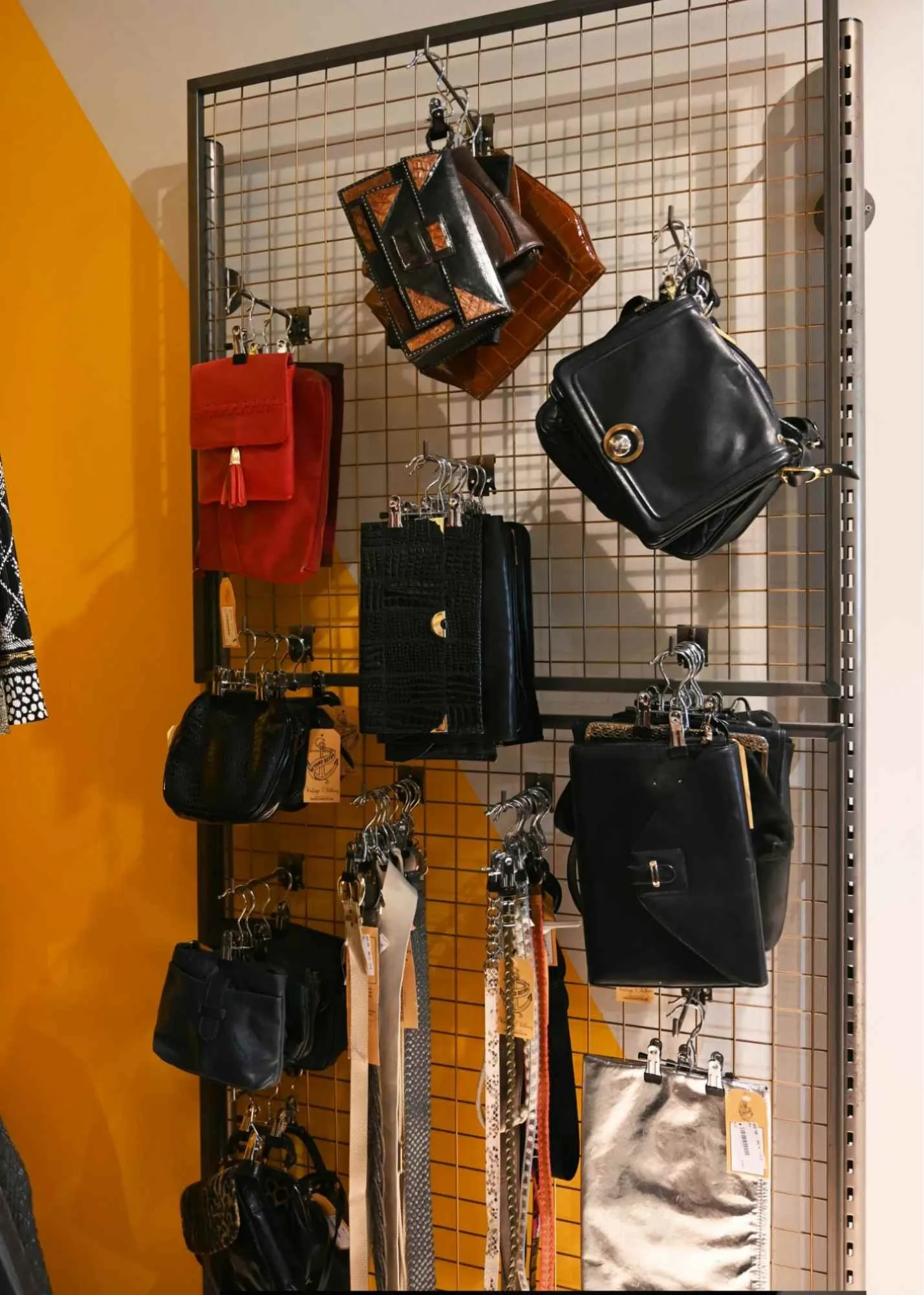 Display of handbags and wallets on a metal grid shelf, with various styles and colors arranged by hooks and shelves, including black, red, and brown designs.