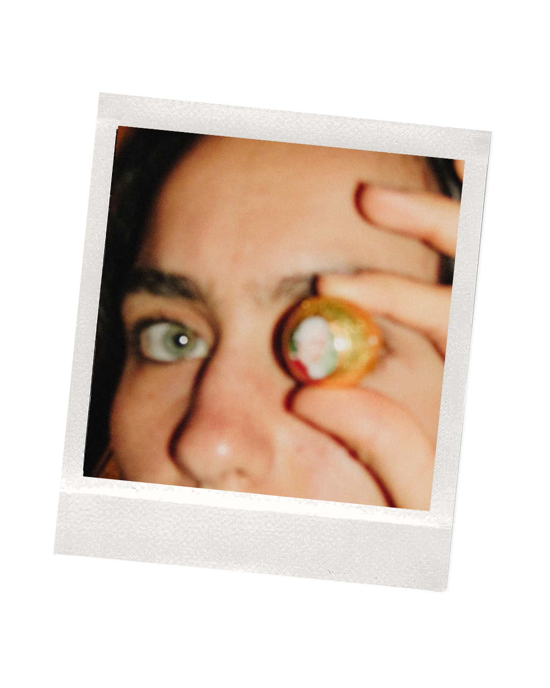 Close-up of a person with blue eyes holding a small, colorful object near their eye.
