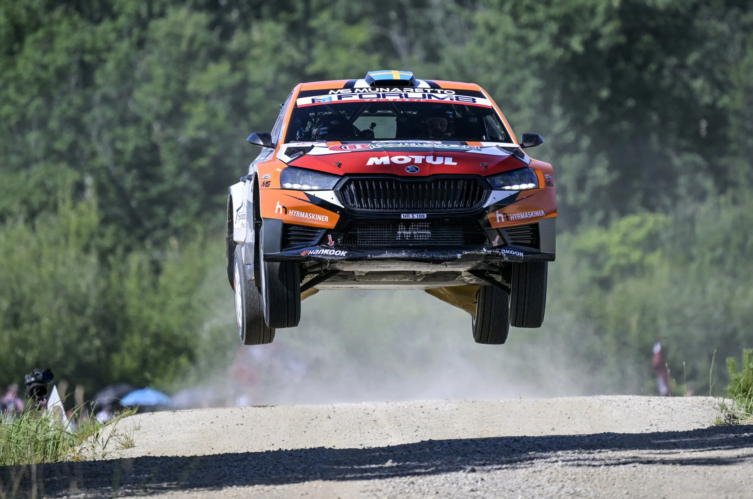 A race car in mid-air during a rally race, with a forested background.