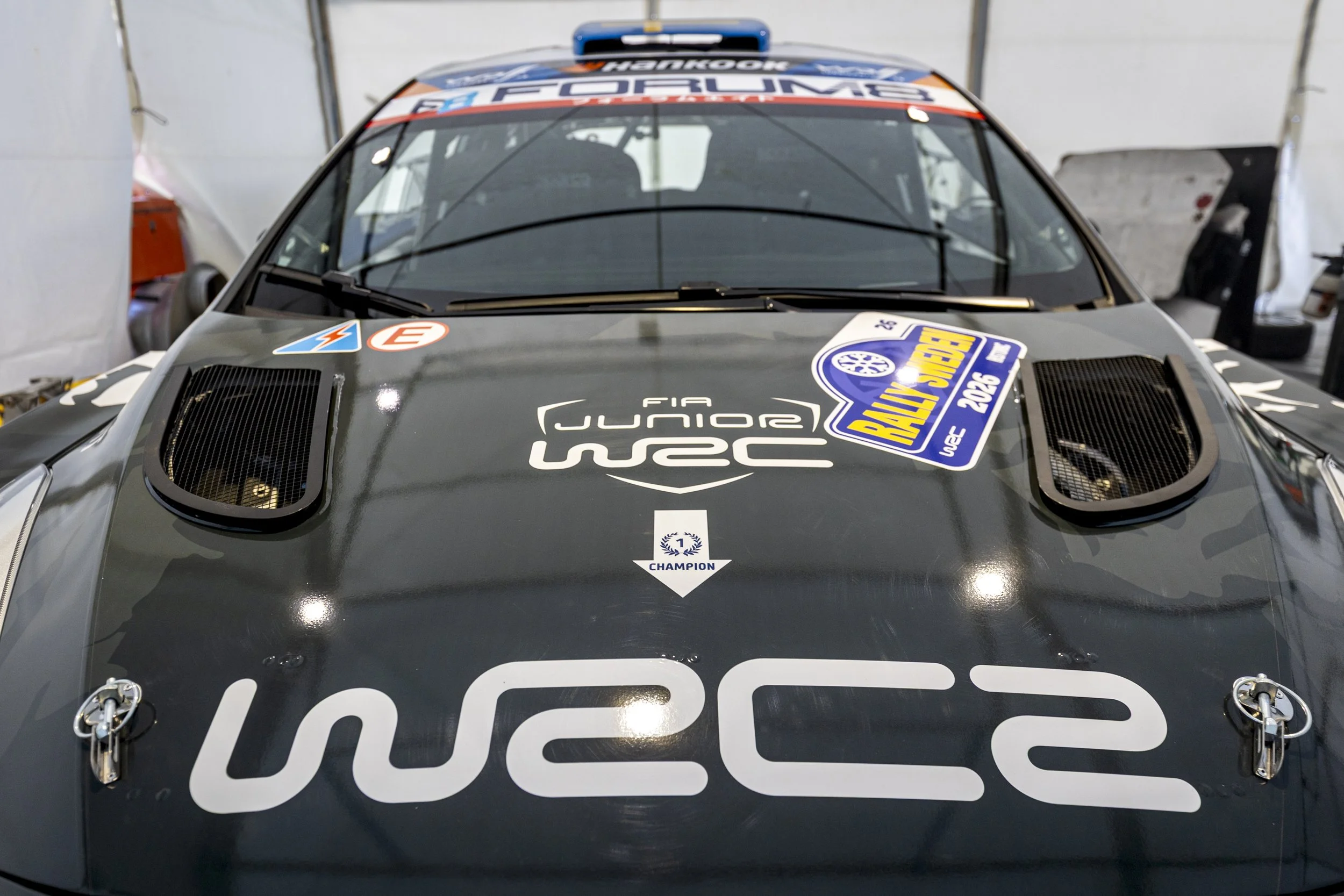 A race car inside a garage with various sponsor logos and racing decals.