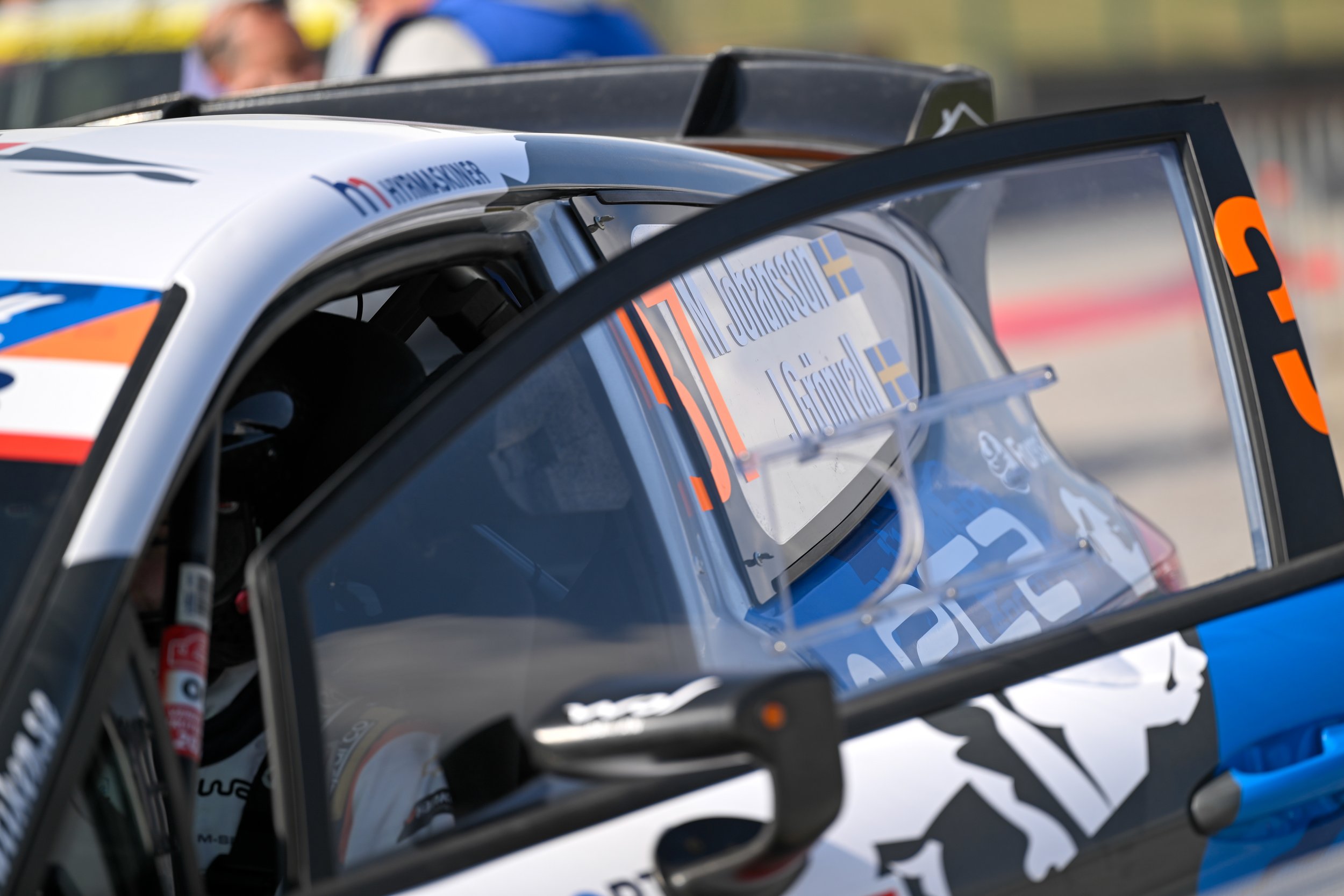 Close-up of a race car with sponsors' stickers on the side window, including Ericsson and Swedish flags, during a motorsport event.