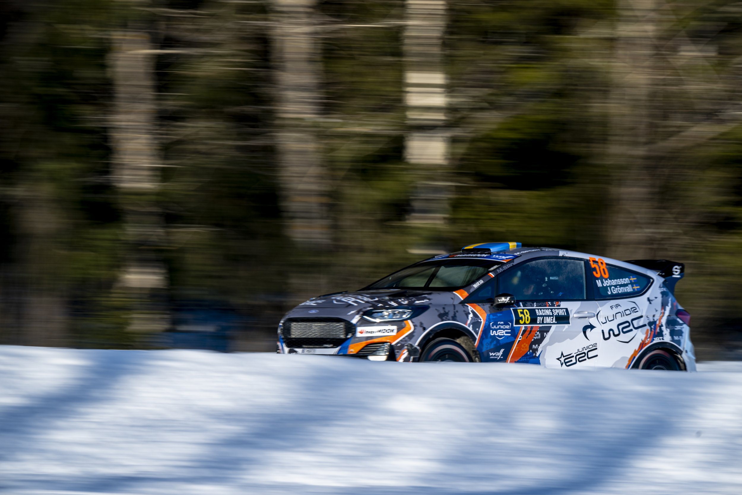 A race car speeding on snow-covered terrain with a blurred forest background.