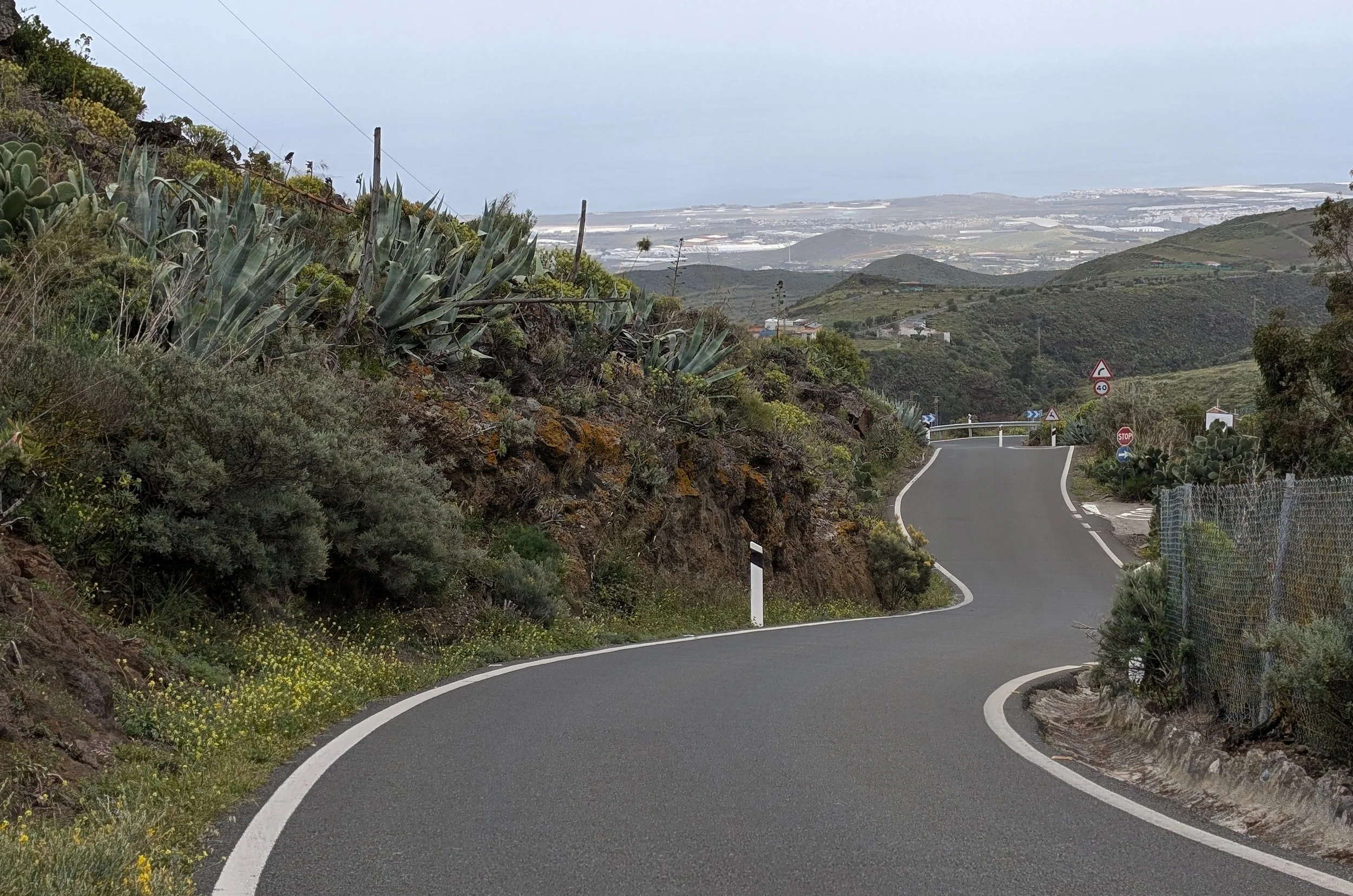 Winding mountain road with green hills and coastal view in the background.