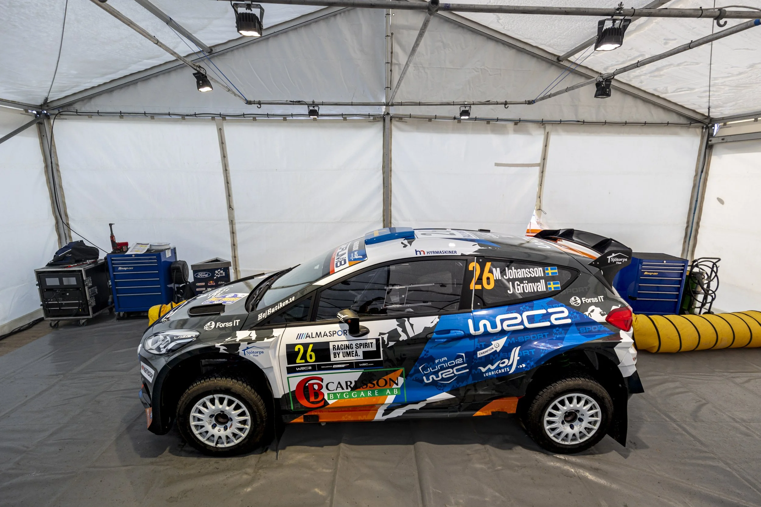 Race car inside a tent with tools and equipment in the background.