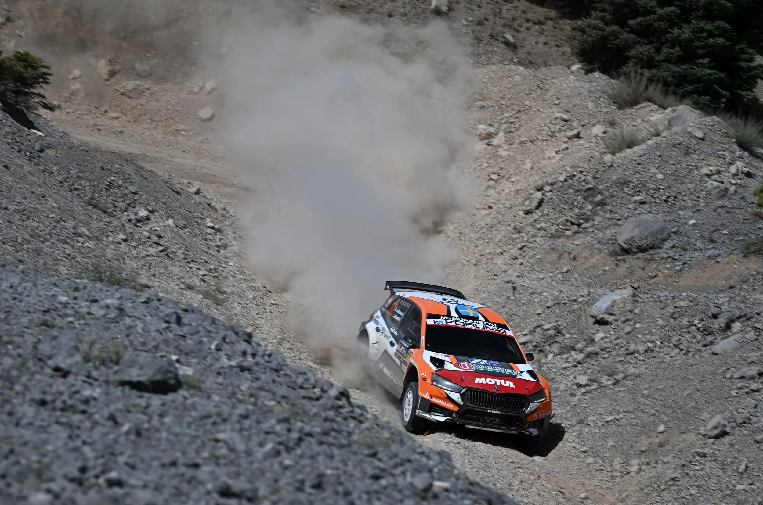 A rally car speeding on a rocky mountain dirt road, kicking up dust and smoke.