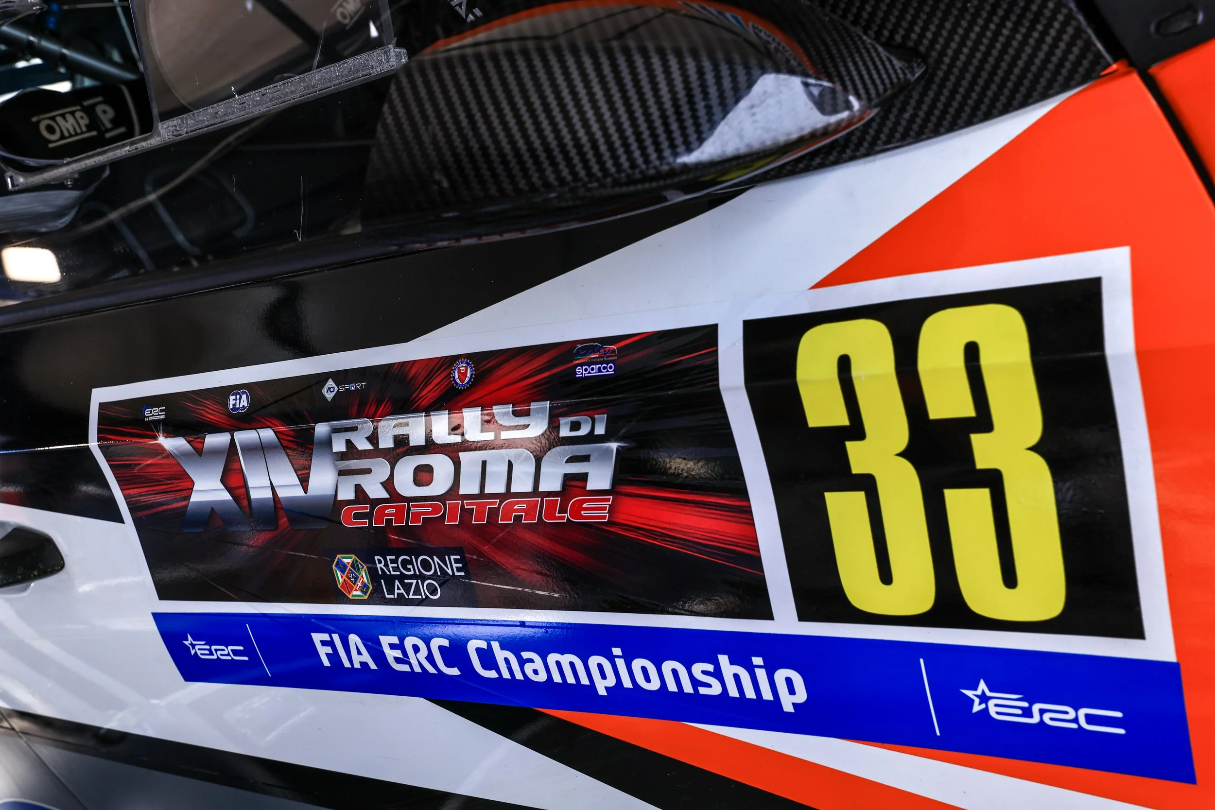 Close-up of a car with rally racing stickers, including logos for FIA, ERC, and Sparco, and the text 'XV Rally di Roma Capitale' and 'FIA ERC Championship'.