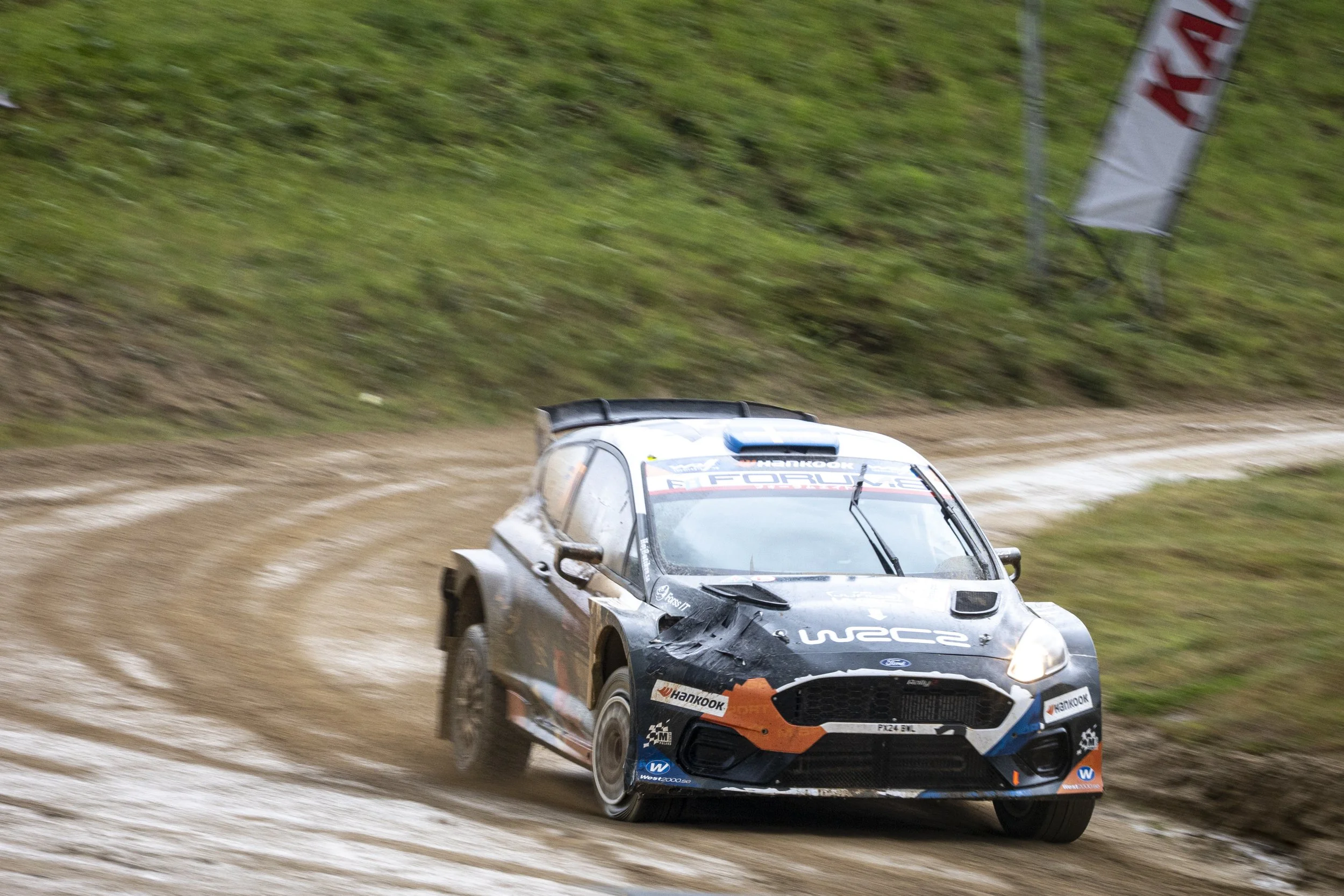 A rally car racing on a dirt track, kicking up dust.