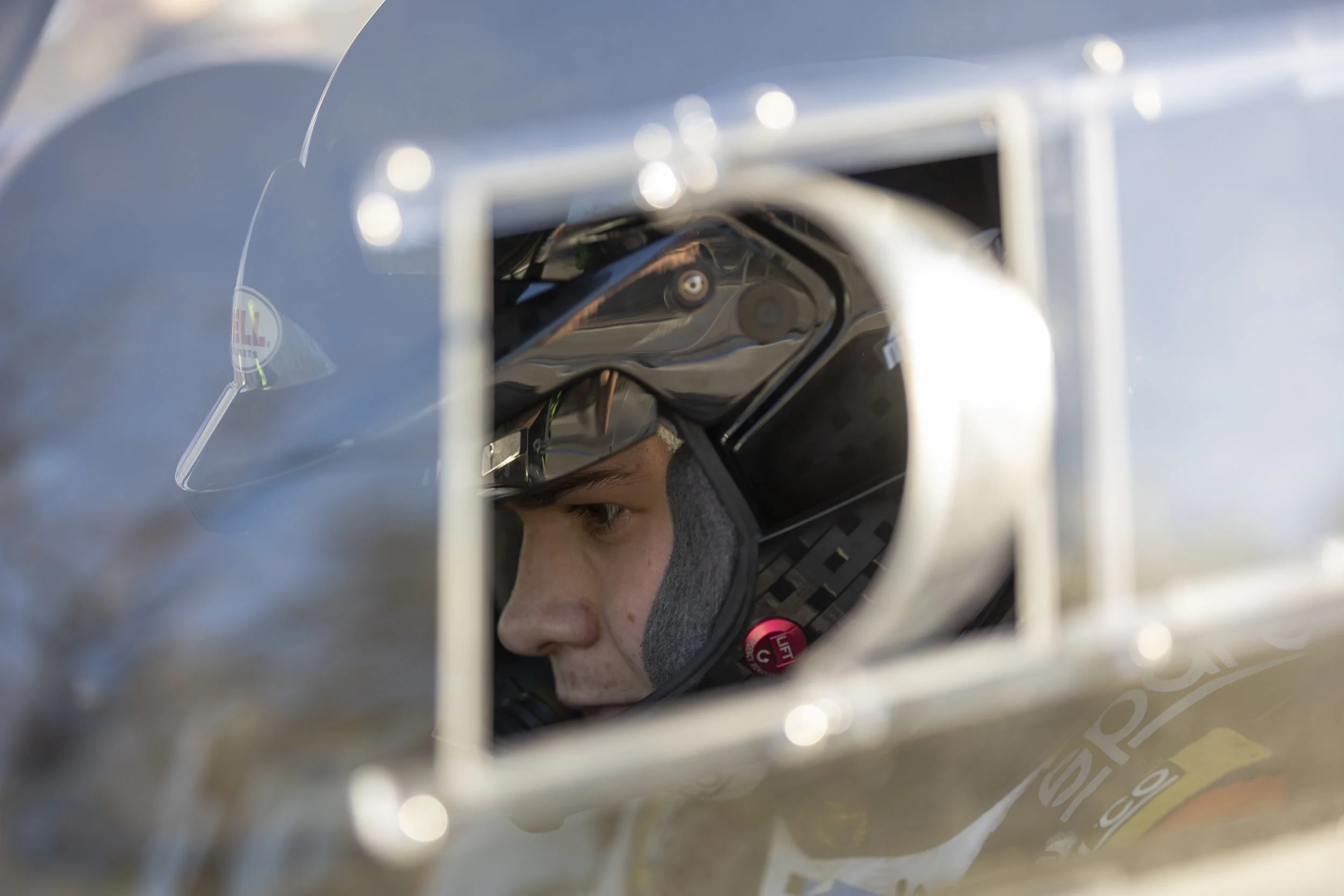 Close-up view of a person wearing a black helmet, looking through a small opening, possibly on a race car or equipment.