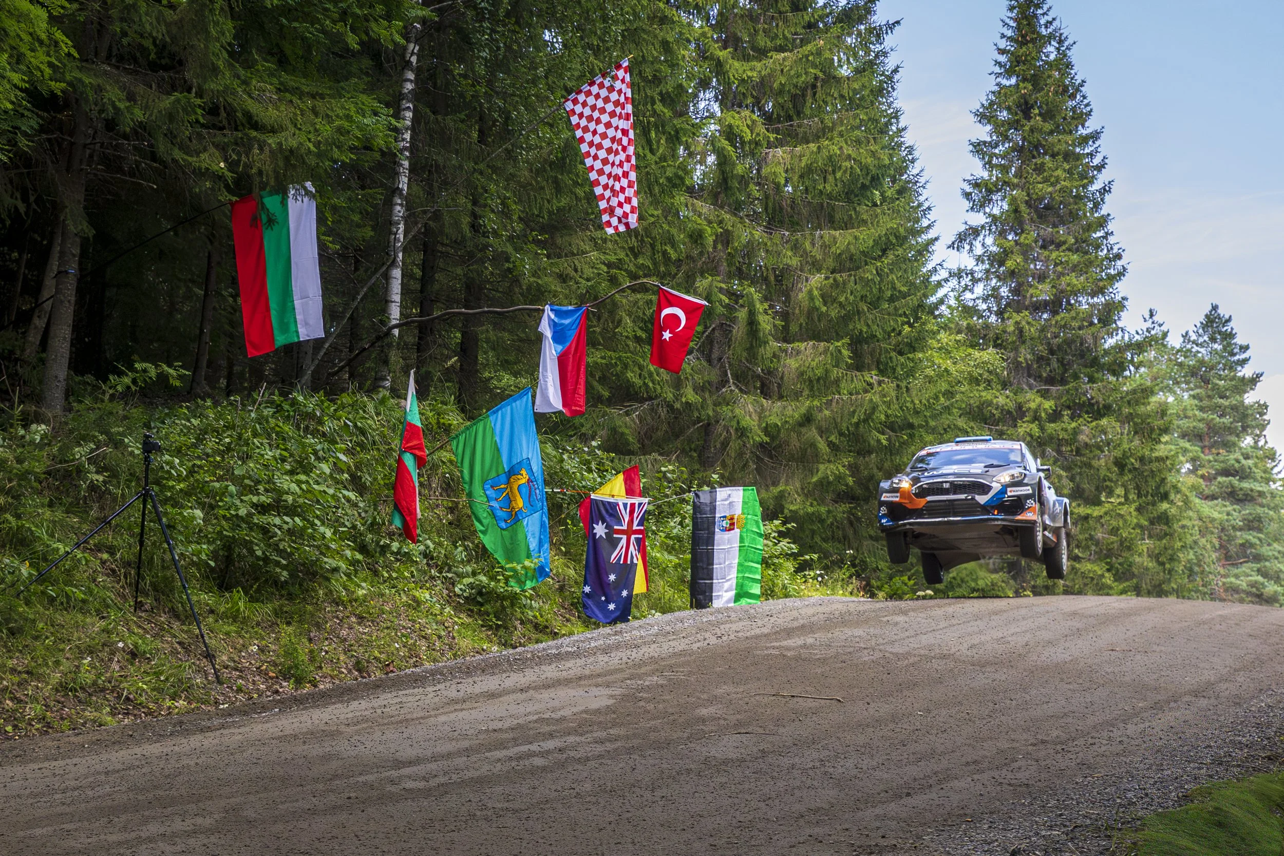 Emergency rally flags on a forest roadside with a black rally car flying in mid-air.