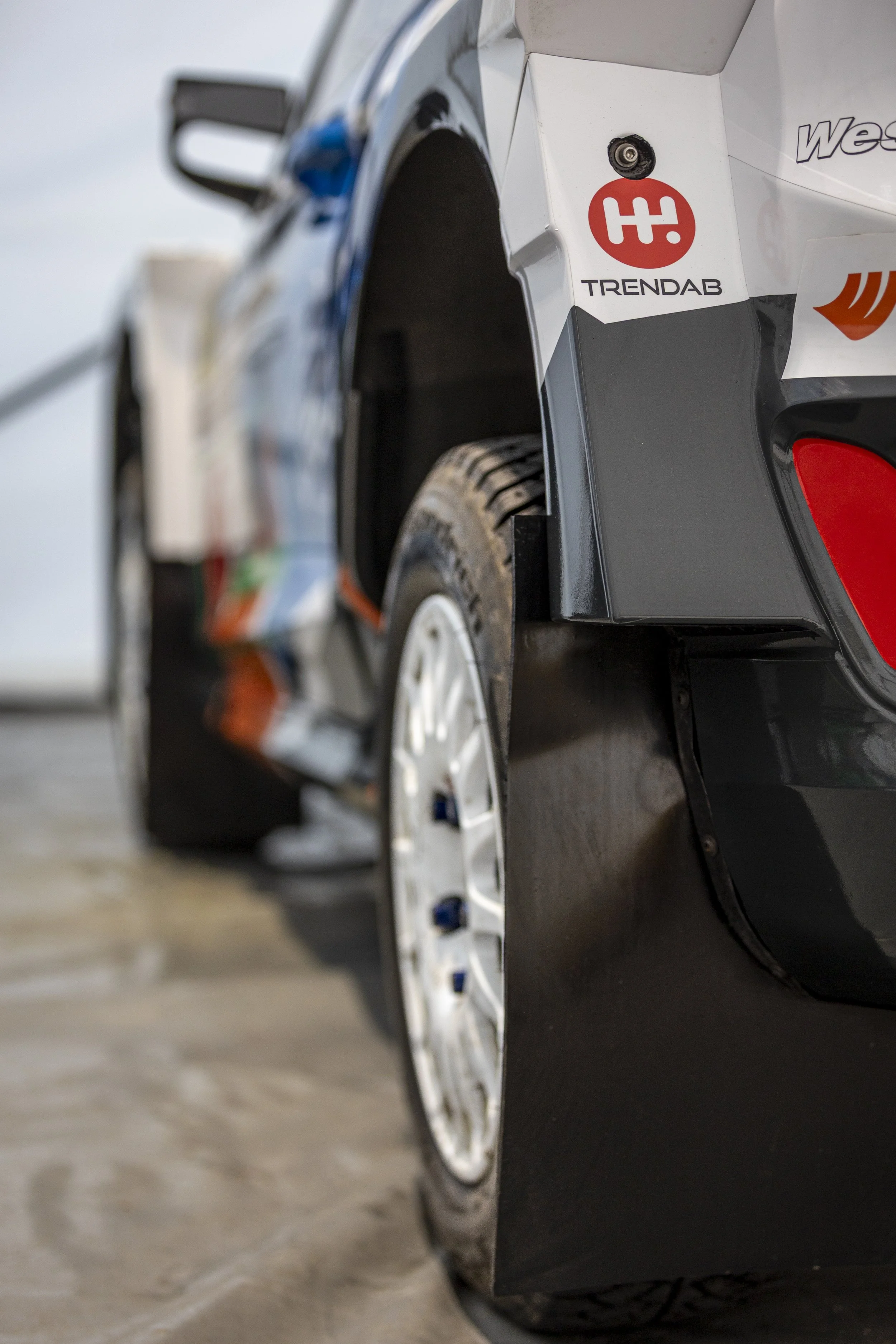Close-up of a car with a Focus TRENDRAB logo on the side. The vehicle's wheel is visible, with some dirt on the tire. The background is slightly blurred.