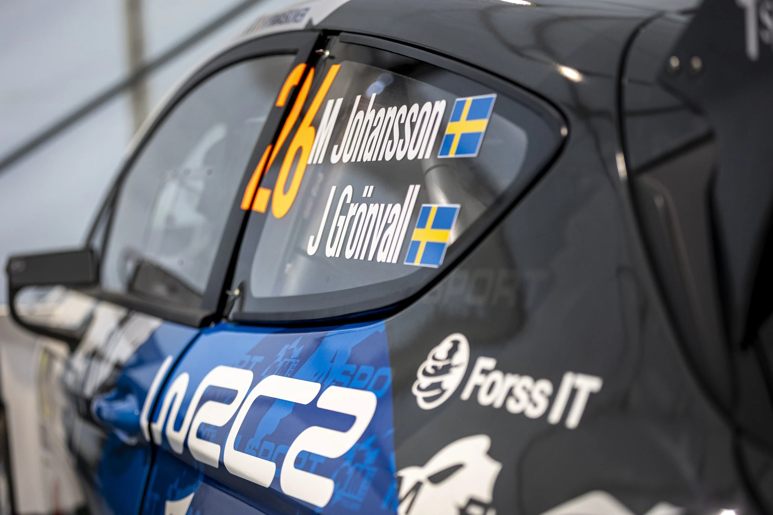Close-up of a racing car window with stickers including the number 16, Swedish flags, and sponsor logos.