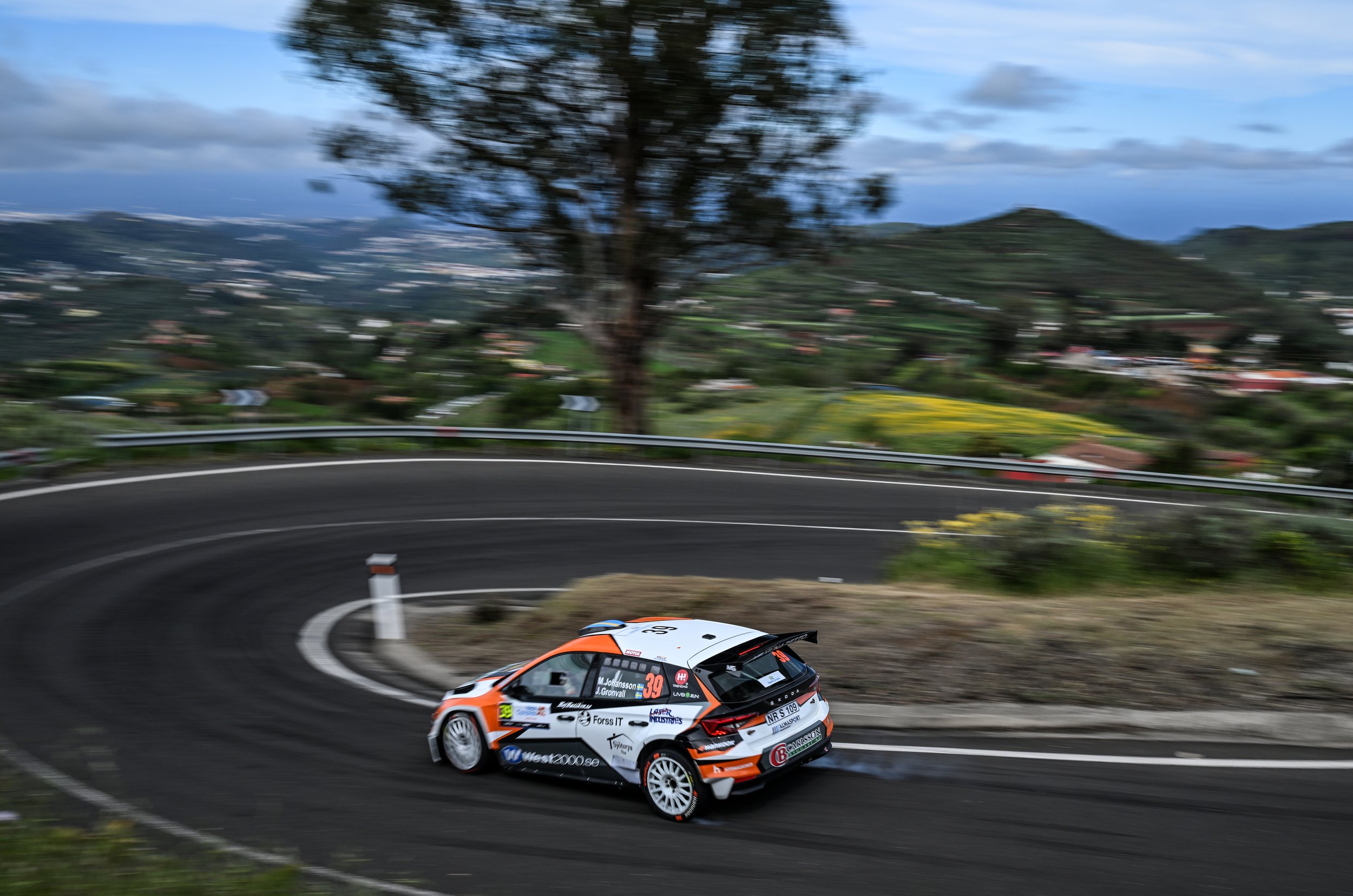 A rally car racing on a winding mountain road with lush green scenery in the background.