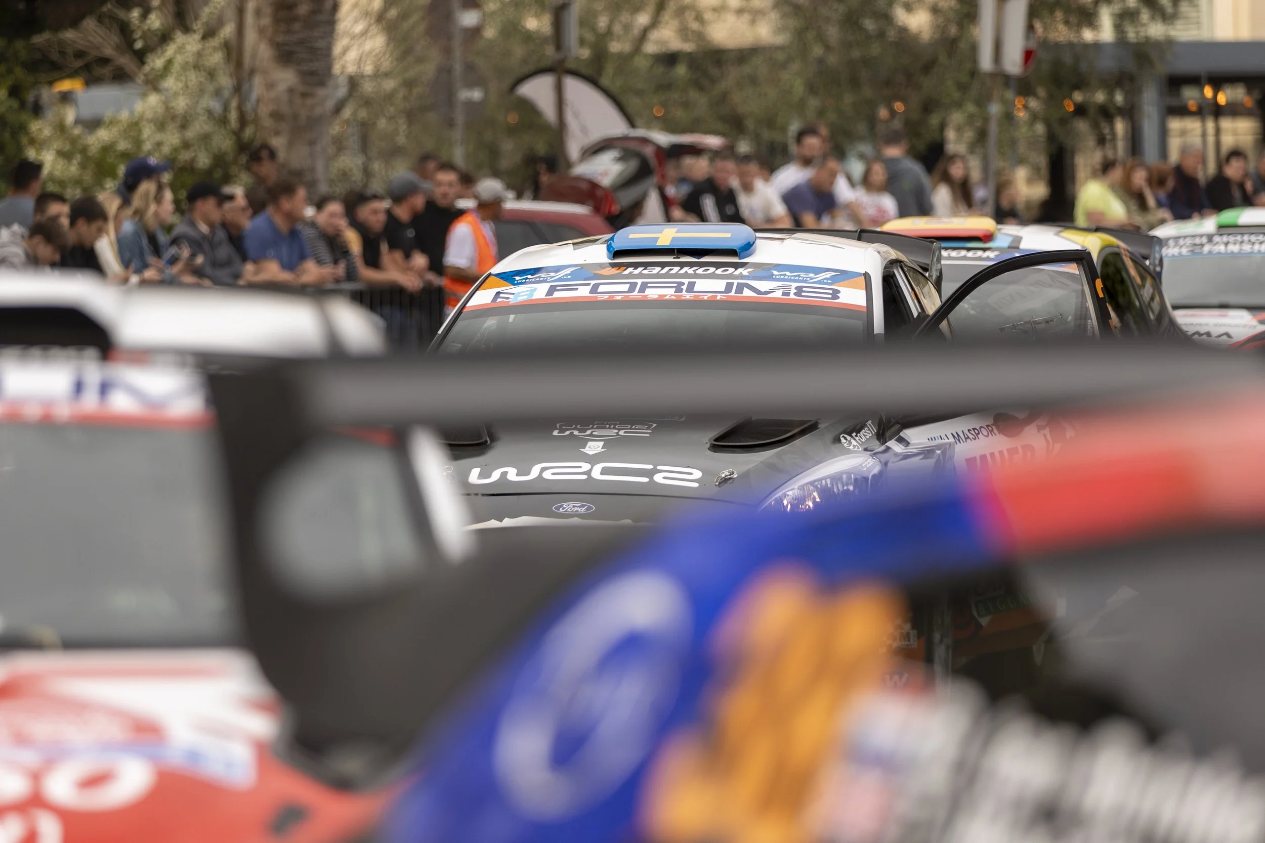 Race cars lined up before a race with spectators and officials in the background.