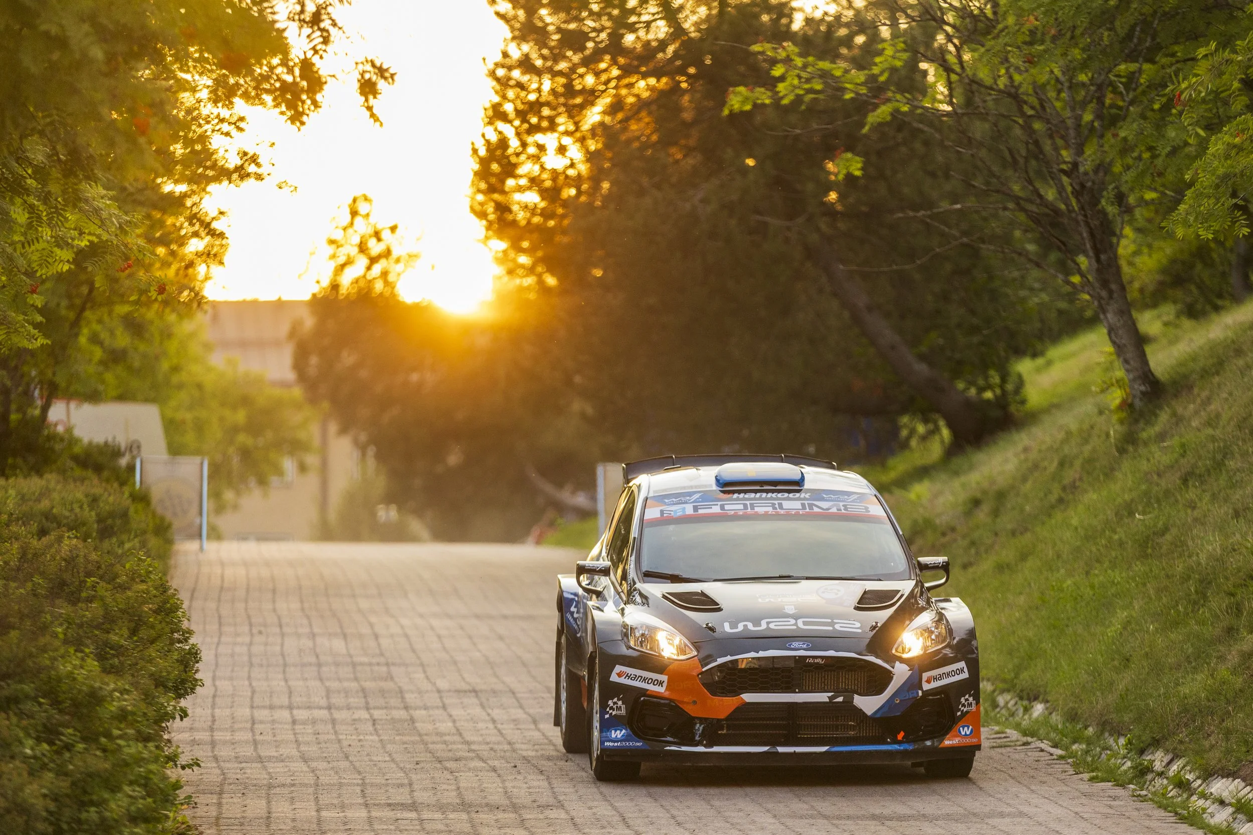 Rally car on a street during sunset with trees on sides.