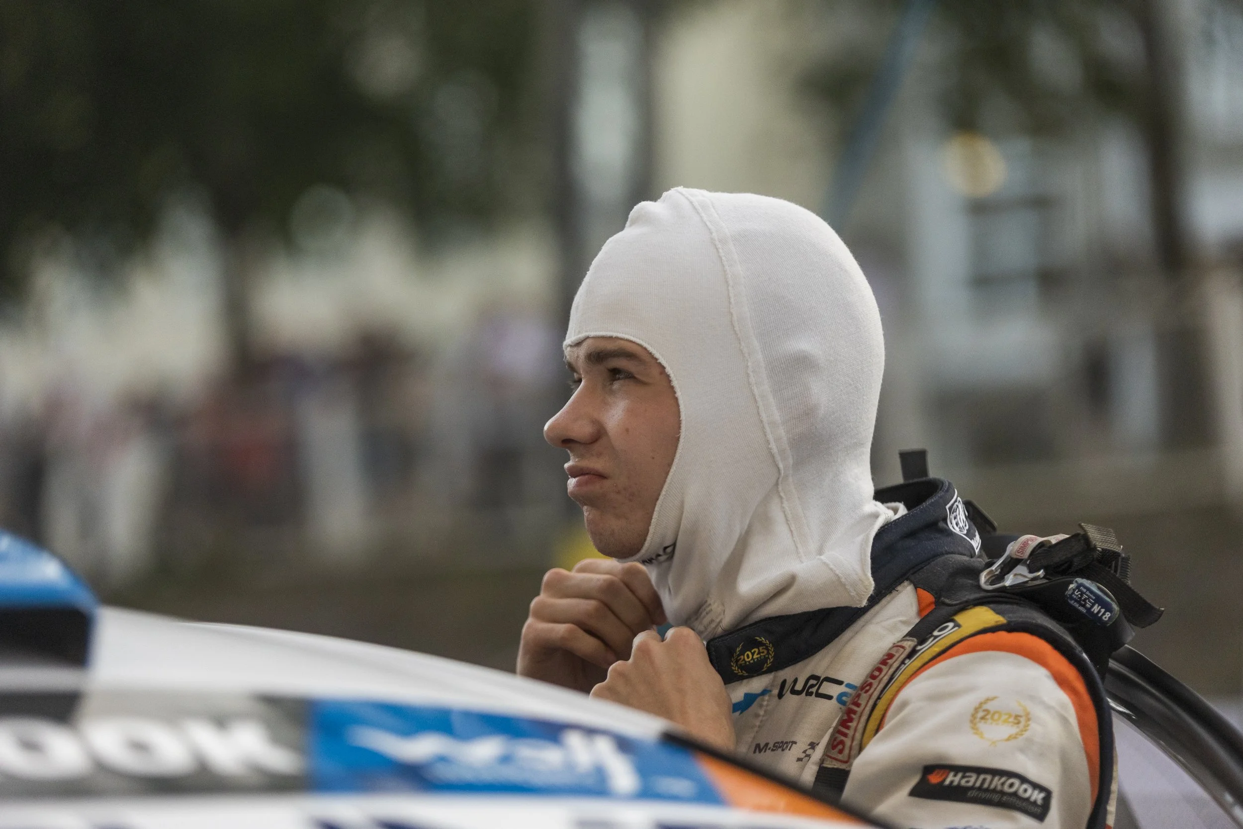 Close-up of a racing driver wearing a white racing helmet and suit, adjusting his gear before a race.