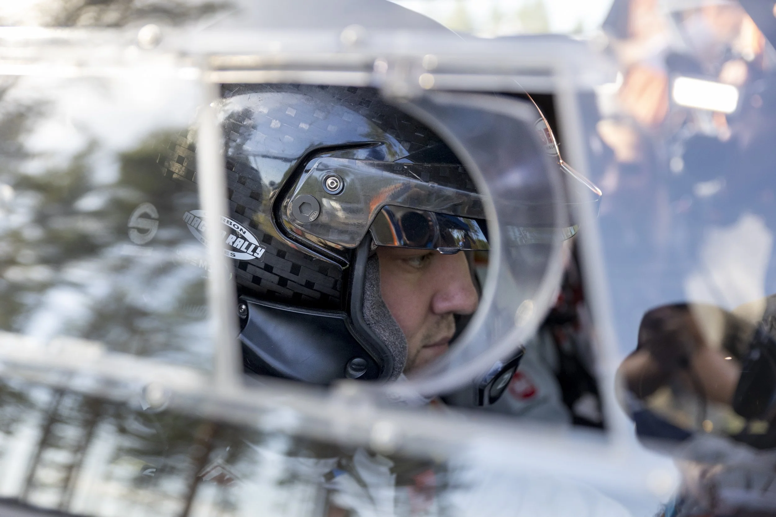 Close-up of a person wearing a helmet, looking ahead with a serious expression, inside a racing vehicle.