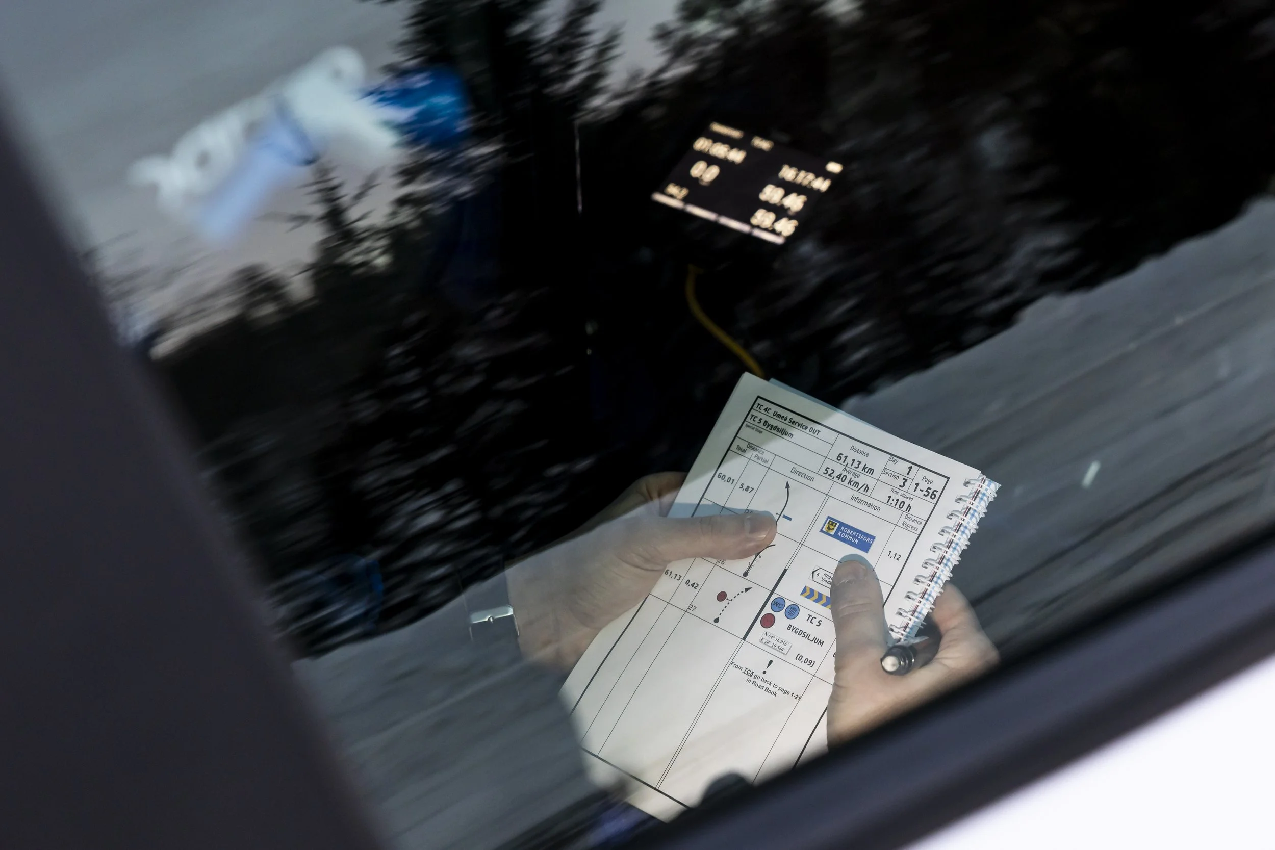 A person holding a traffic or navigation card with a map and details, seen through a car window with a reflection of trees.