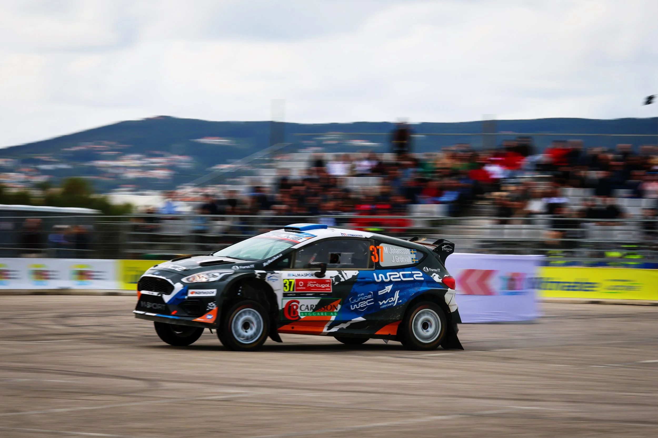 Race car speeding on a racetrack with a blurred background of spectators and hills.